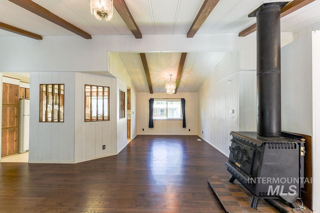 Unfurnished living room with a wood stove, dark wood-type flooring, beamed ceiling, wood walls, and a chandelier