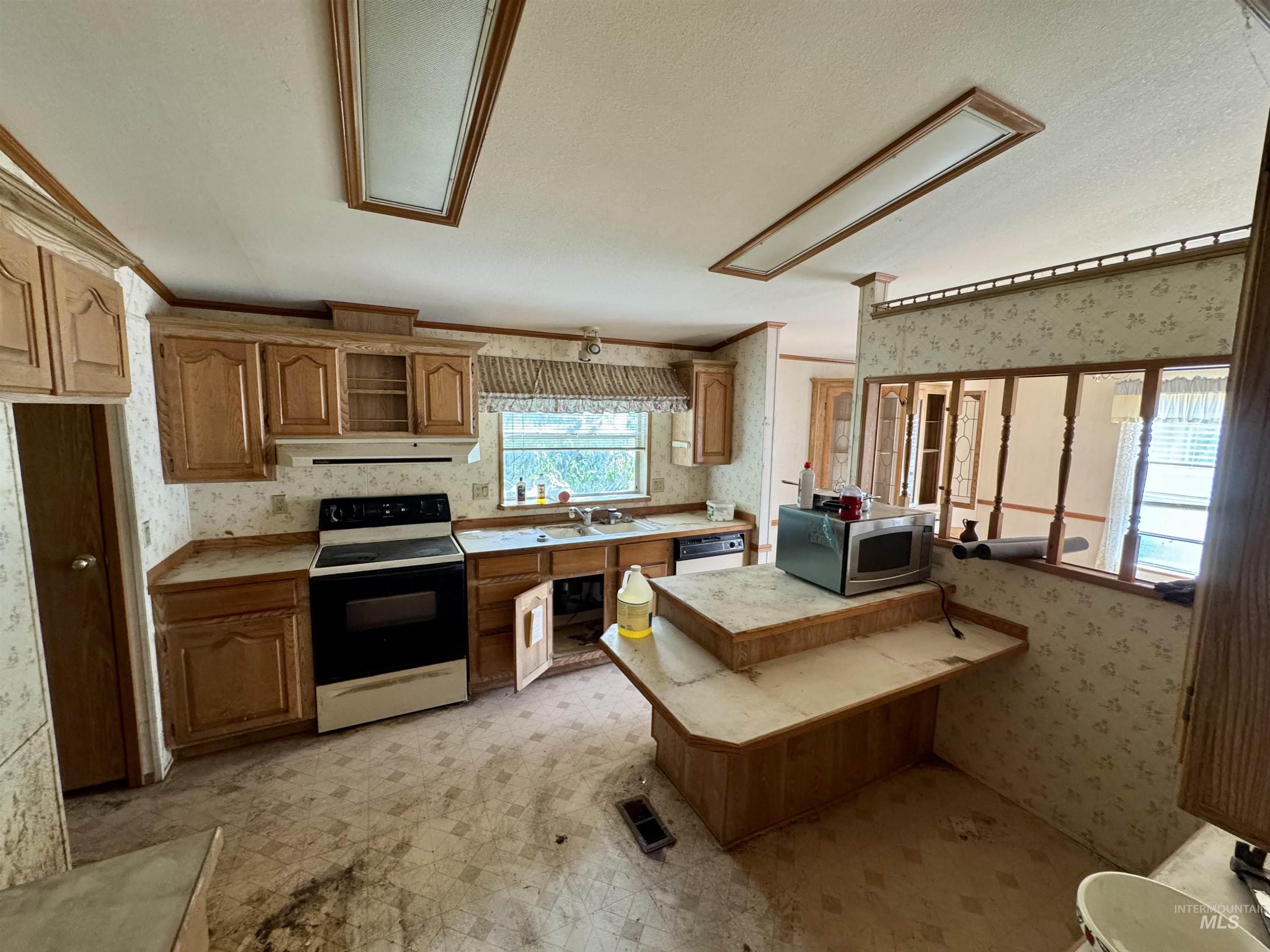 Kitchen featuring wallpapered walls, light countertops, electric stove, brown cabinetry, and stainless steel microwave