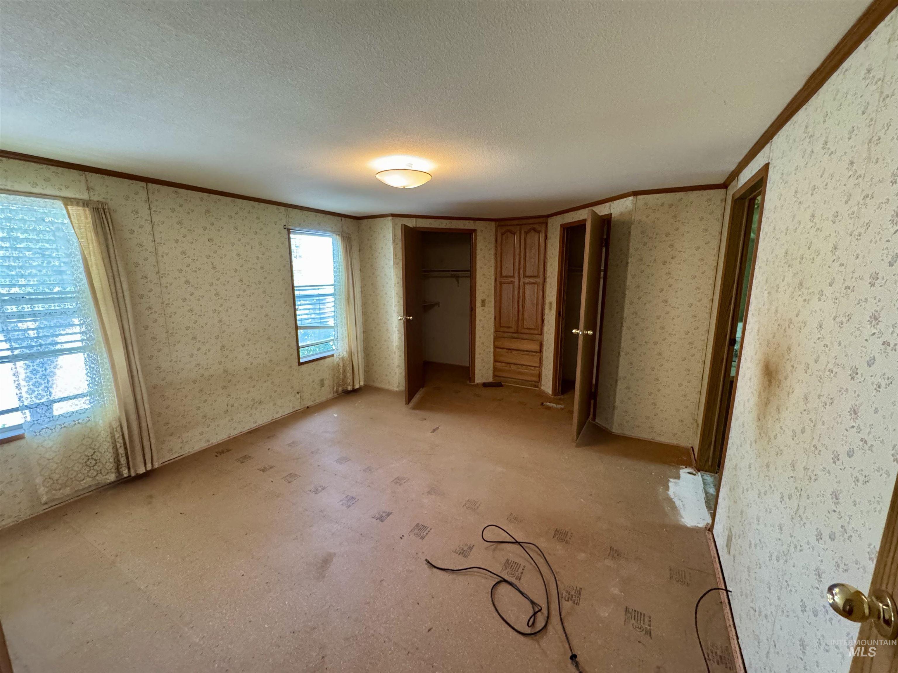 Unfurnished bedroom featuring a closet, ornamental molding, a textured ceiling, and wallpapered walls