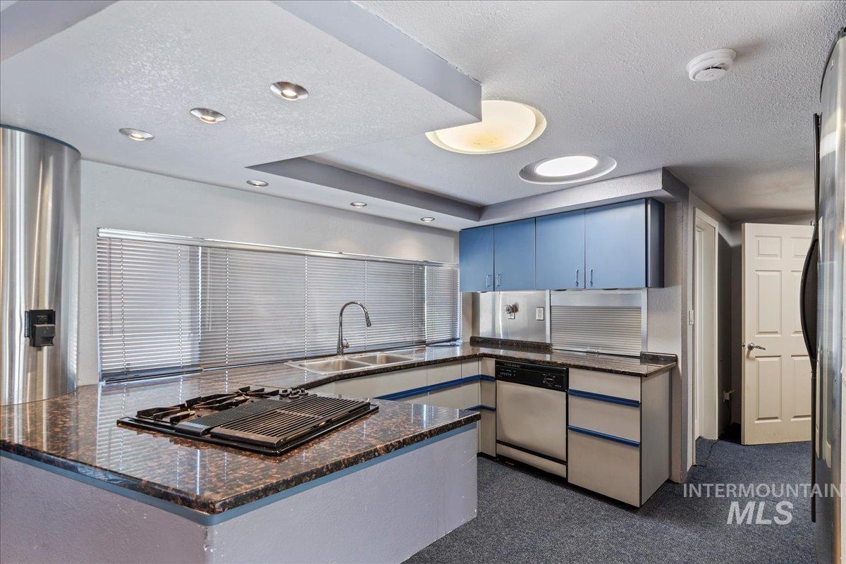Kitchen featuring a textured ceiling, a peninsula, dishwashing machine, black gas stovetop, and dark stone counters