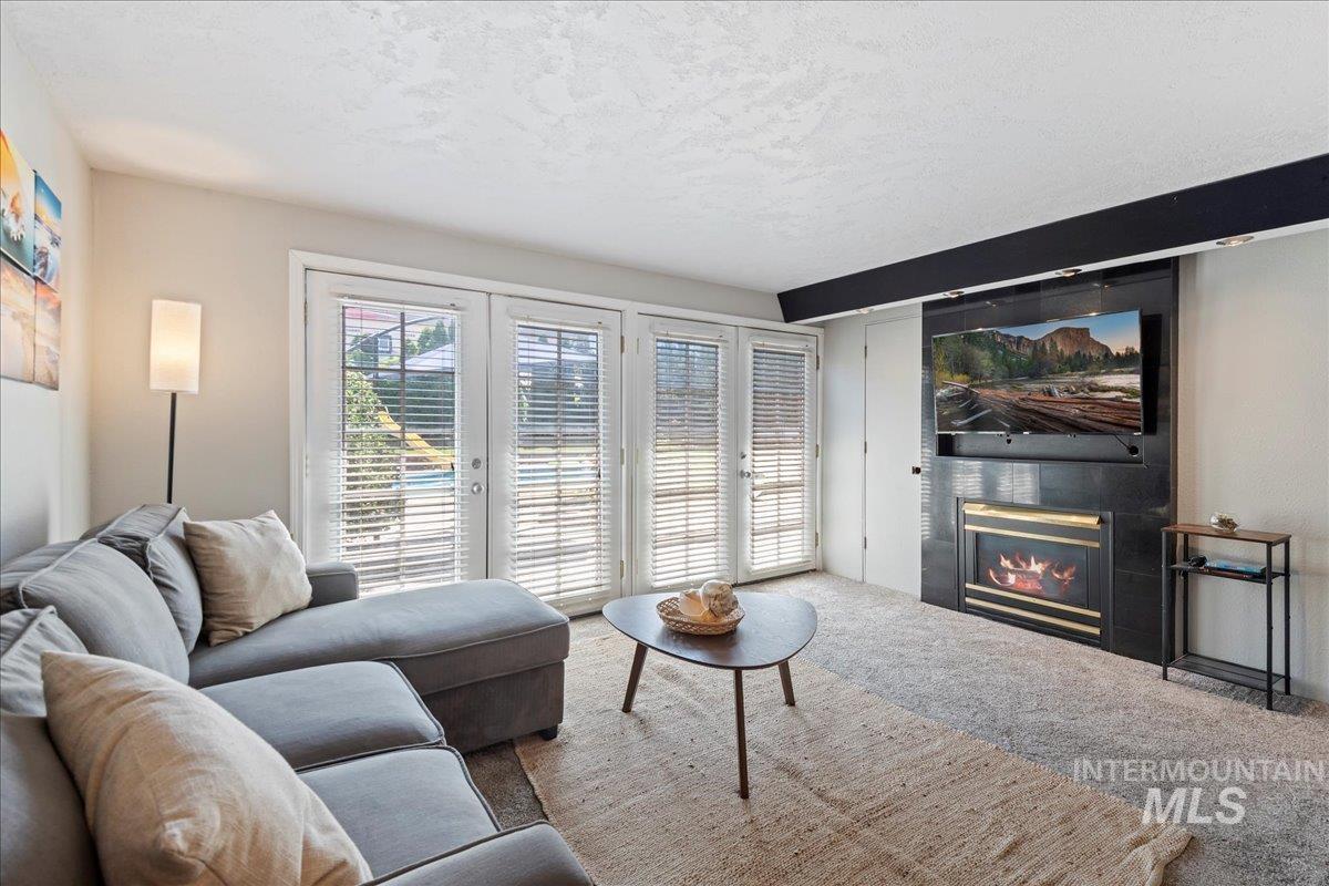 Living area featuring a textured ceiling, carpet, french doors, and a large fireplace