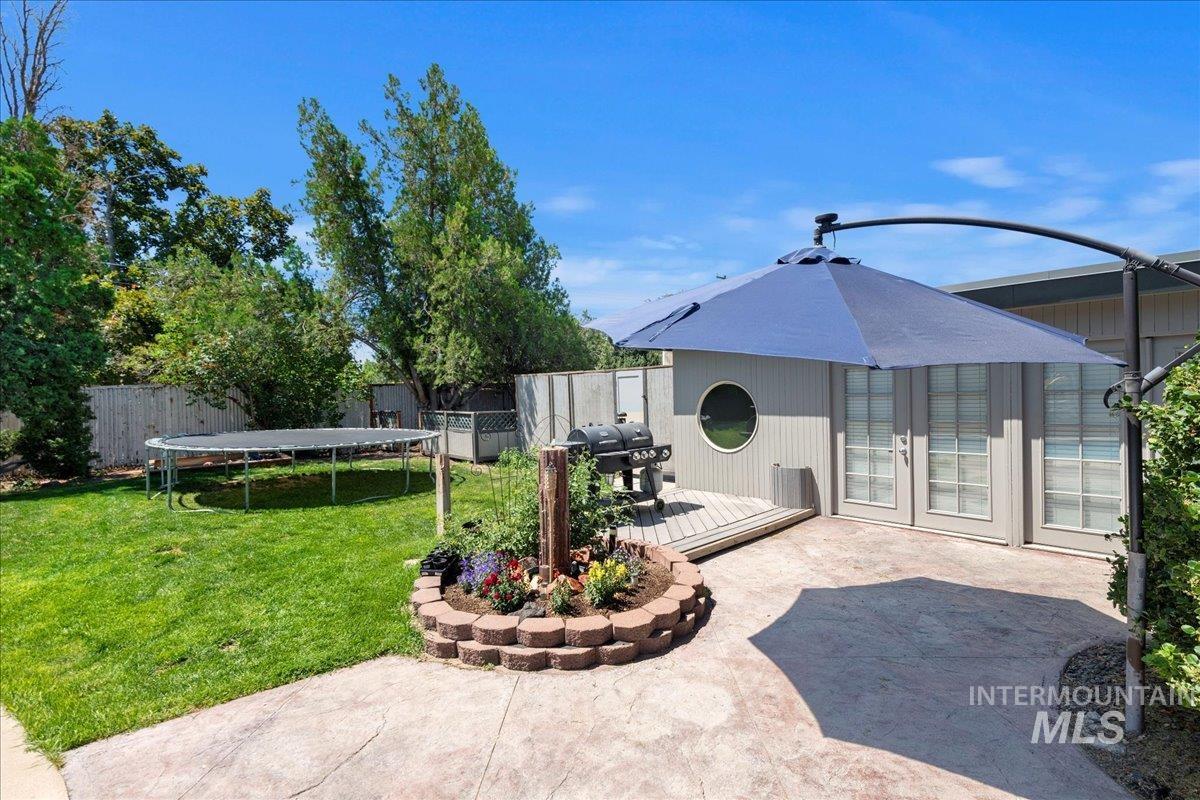 Fenced backyard featuring a trampoline, a wooden deck, french doors, and grilling area