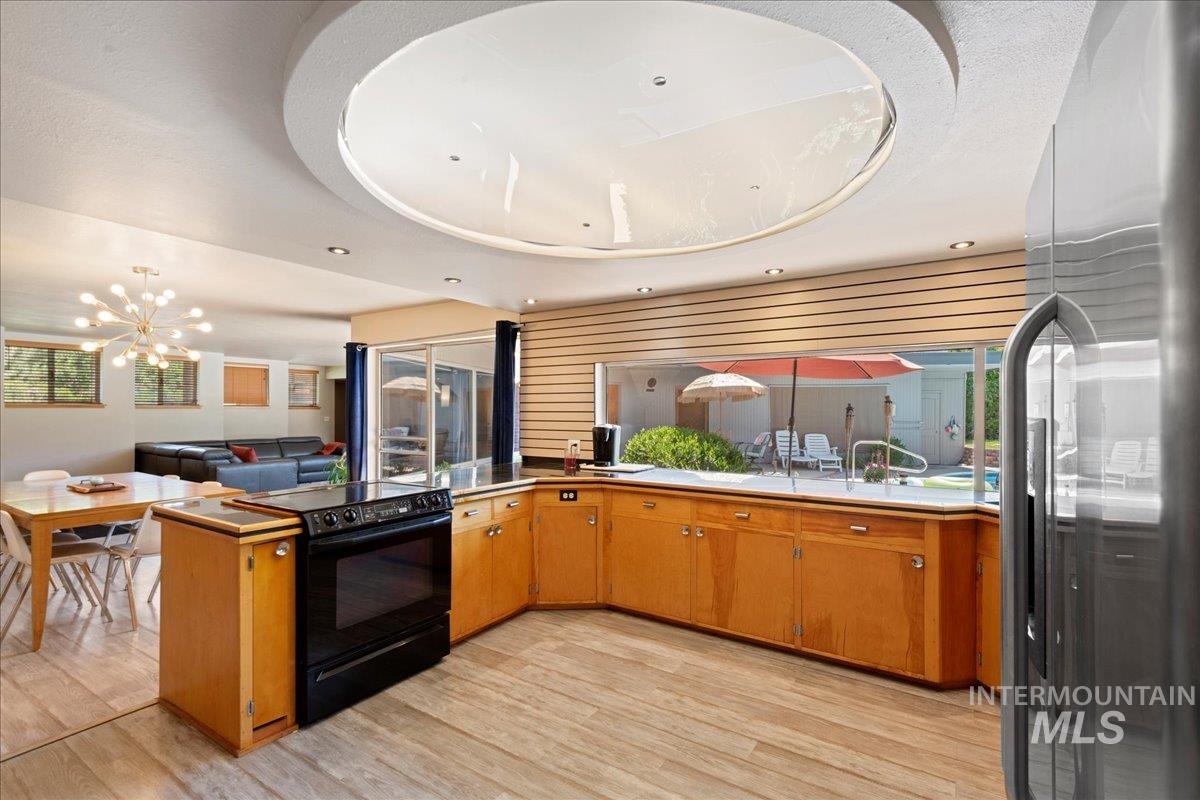 Kitchen featuring stainless steel refrigerator with ice dispenser, electric range, brown cabinetry, light wood finished floors, and light countertops