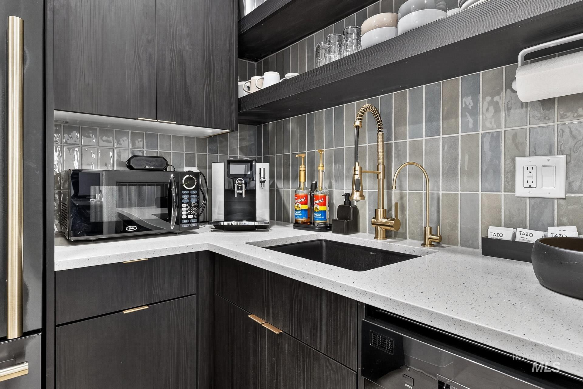 Kitchen with light stone counters, tasteful backsplash, dishwasher, and black microwave