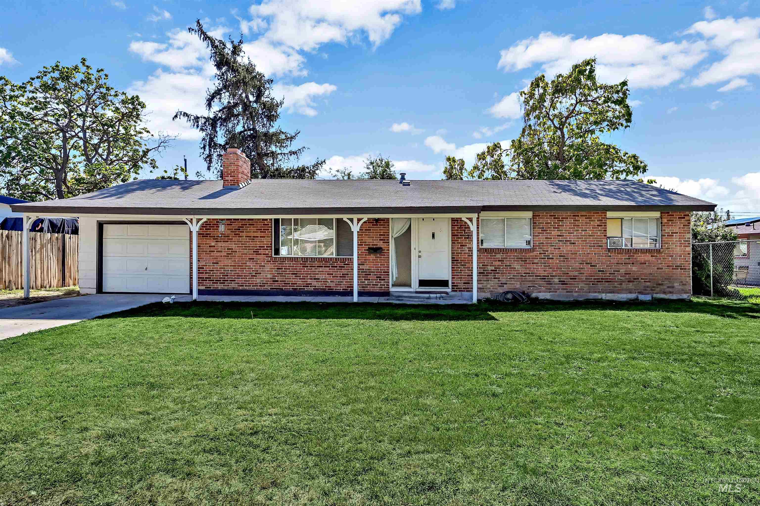 Ranch-style house featuring a chimney, brick siding, a garage, driveway, and a porch
