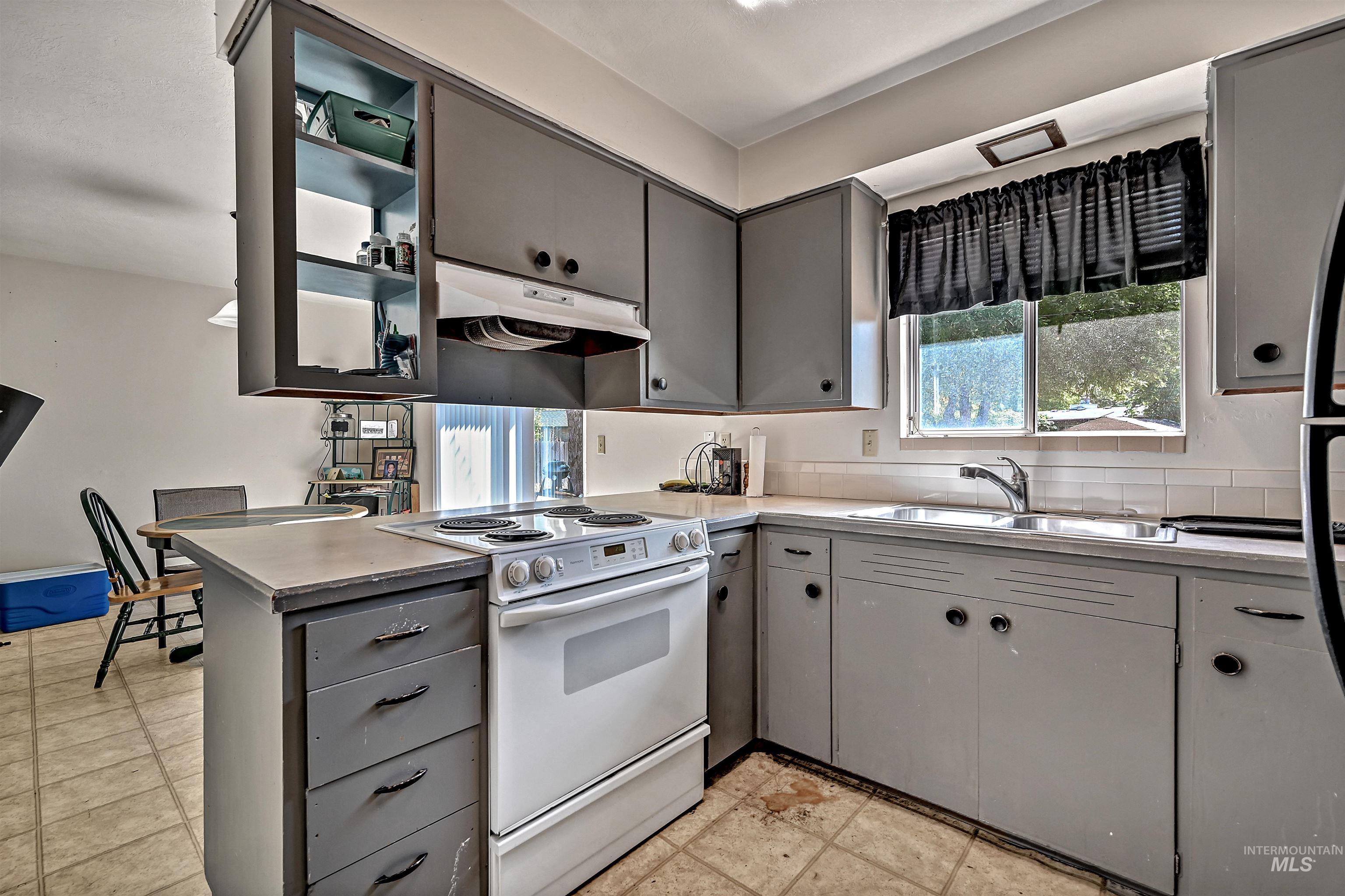 Kitchen with gray cabinetry, white range with electric cooktop, under cabinet range hood, glass insert cabinets, and a peninsula