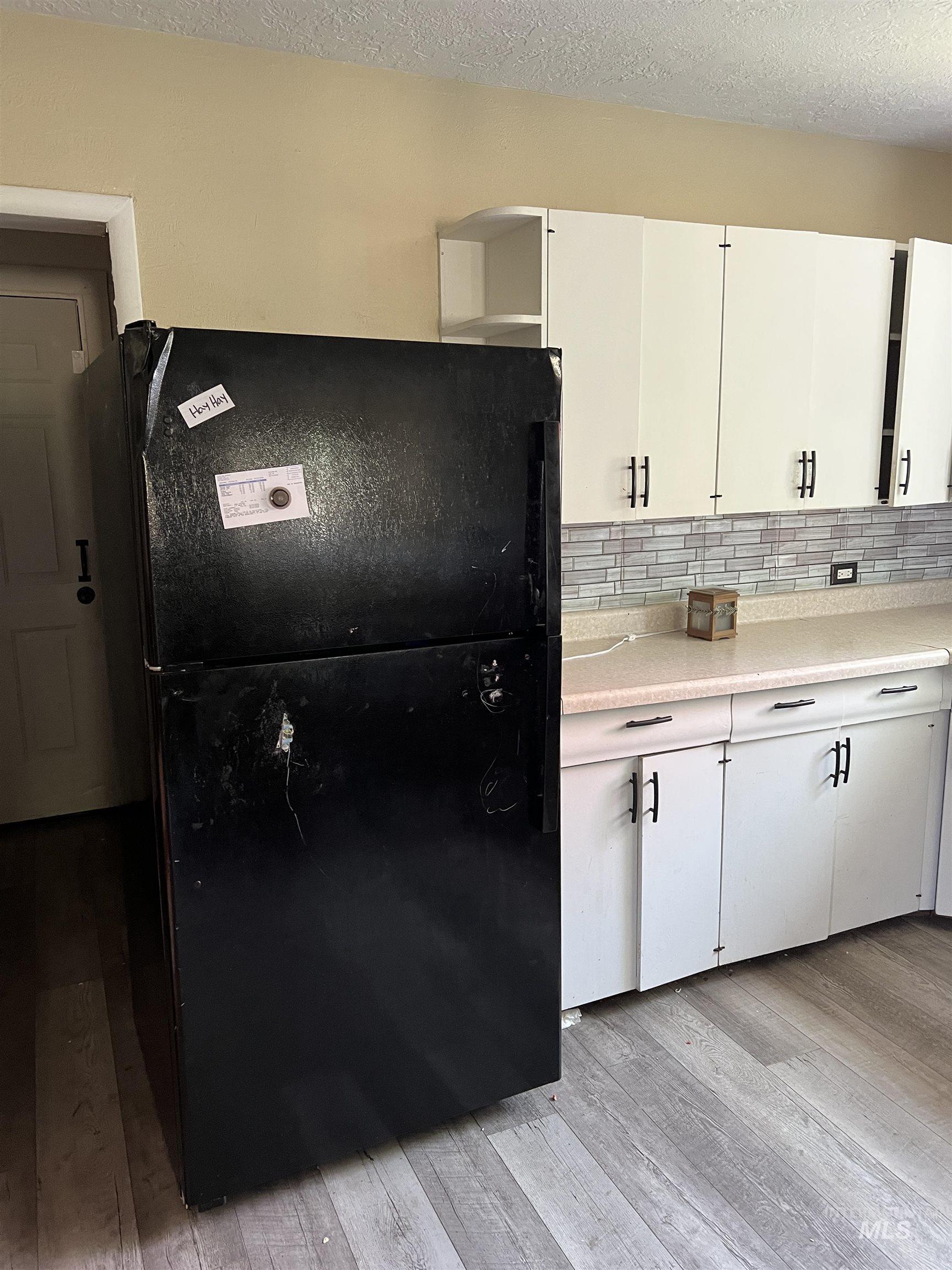 Kitchen featuring freestanding refrigerator, light wood finished floors, light countertops, white cabinets, and backsplash