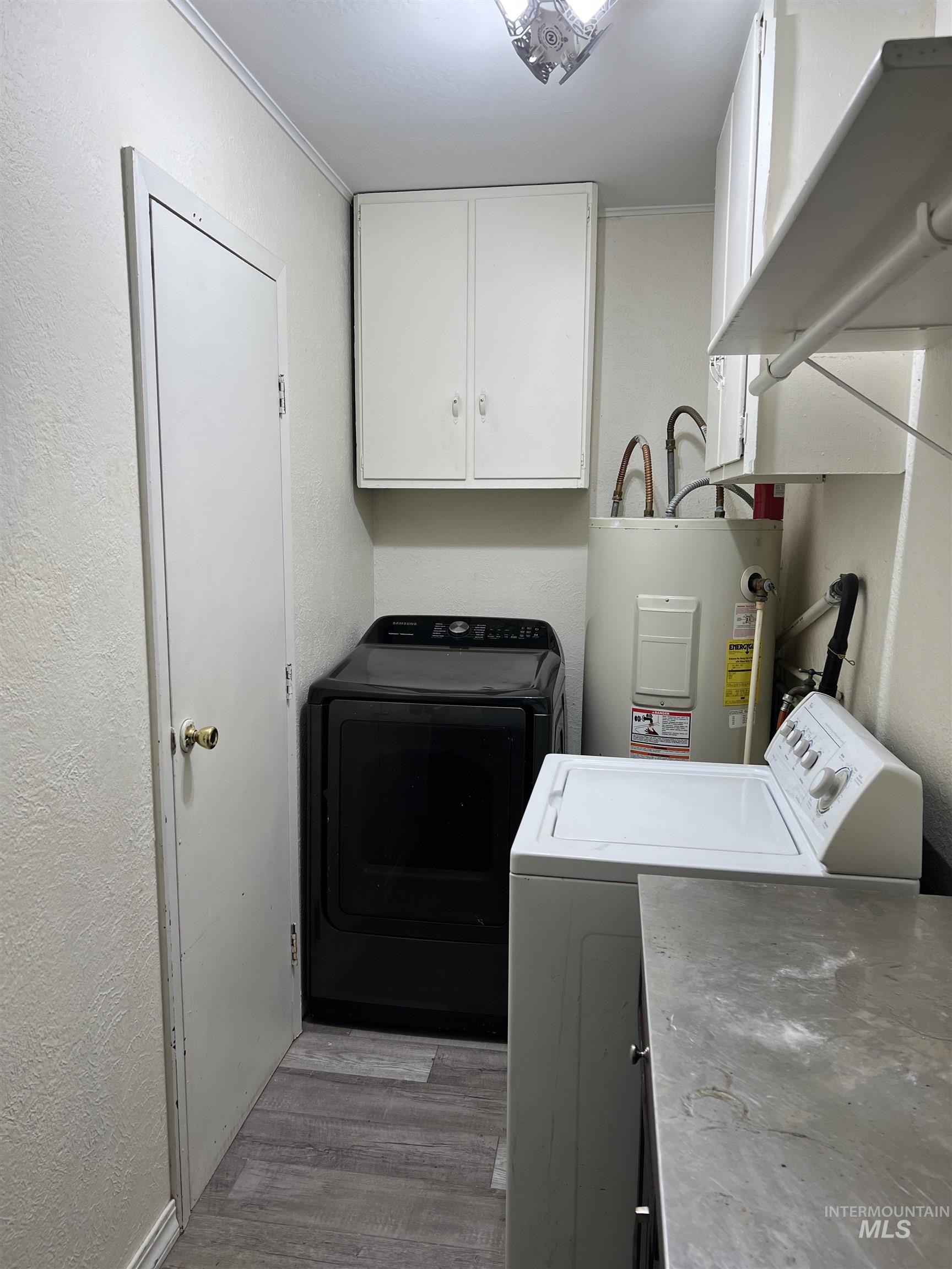 Laundry area featuring electric water heater, cabinet space, washer and dryer, and light wood finished floors