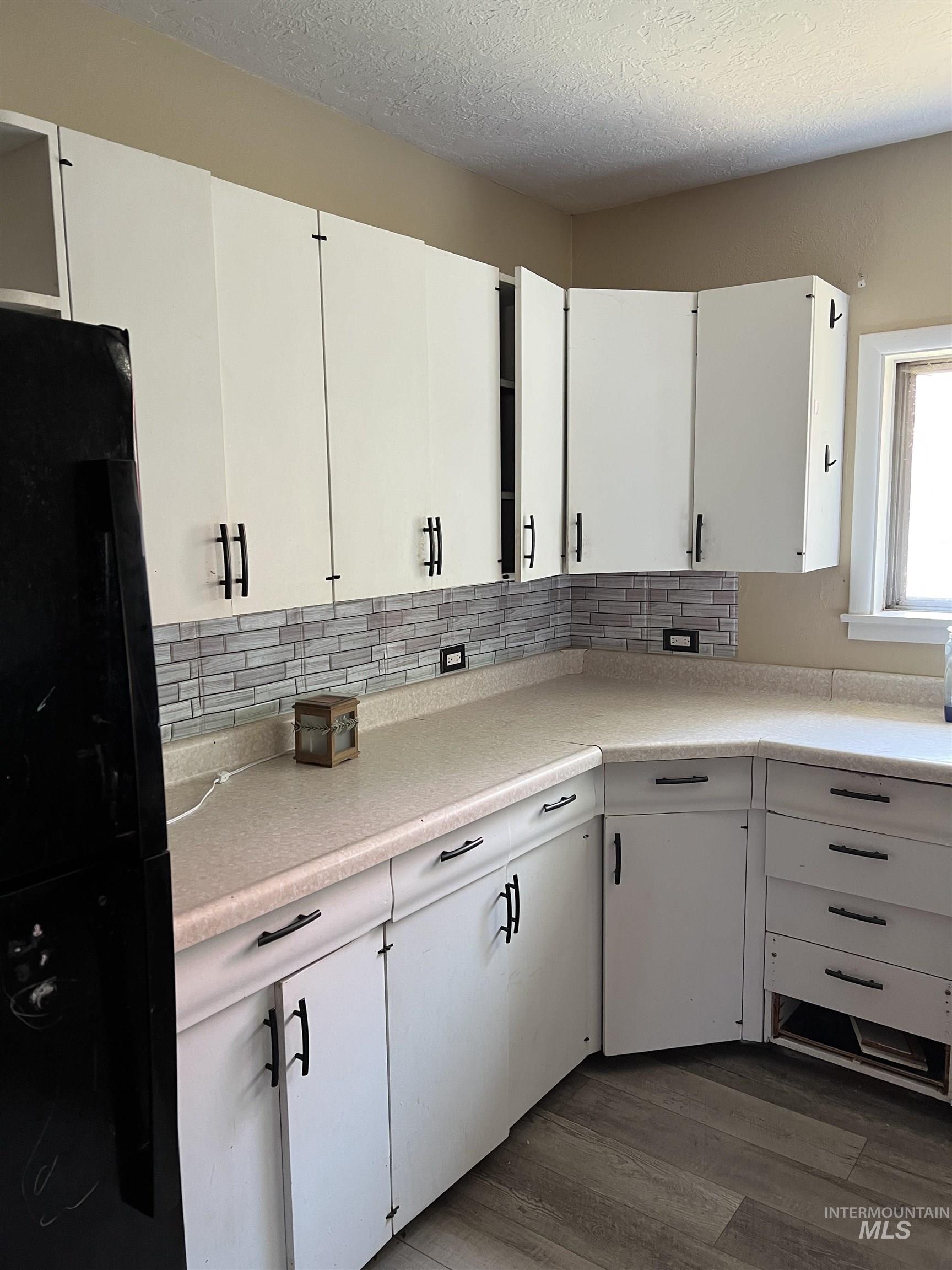Kitchen featuring freestanding refrigerator, backsplash, dark wood-type flooring, light countertops, and white cabinets