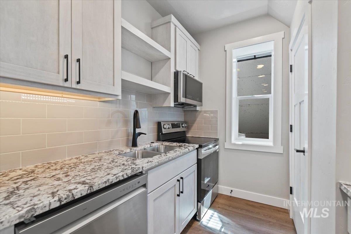 Kitchen with stainless steel appliances, open shelves, dark wood finished floors, light stone countertops, and decorative backsplash
