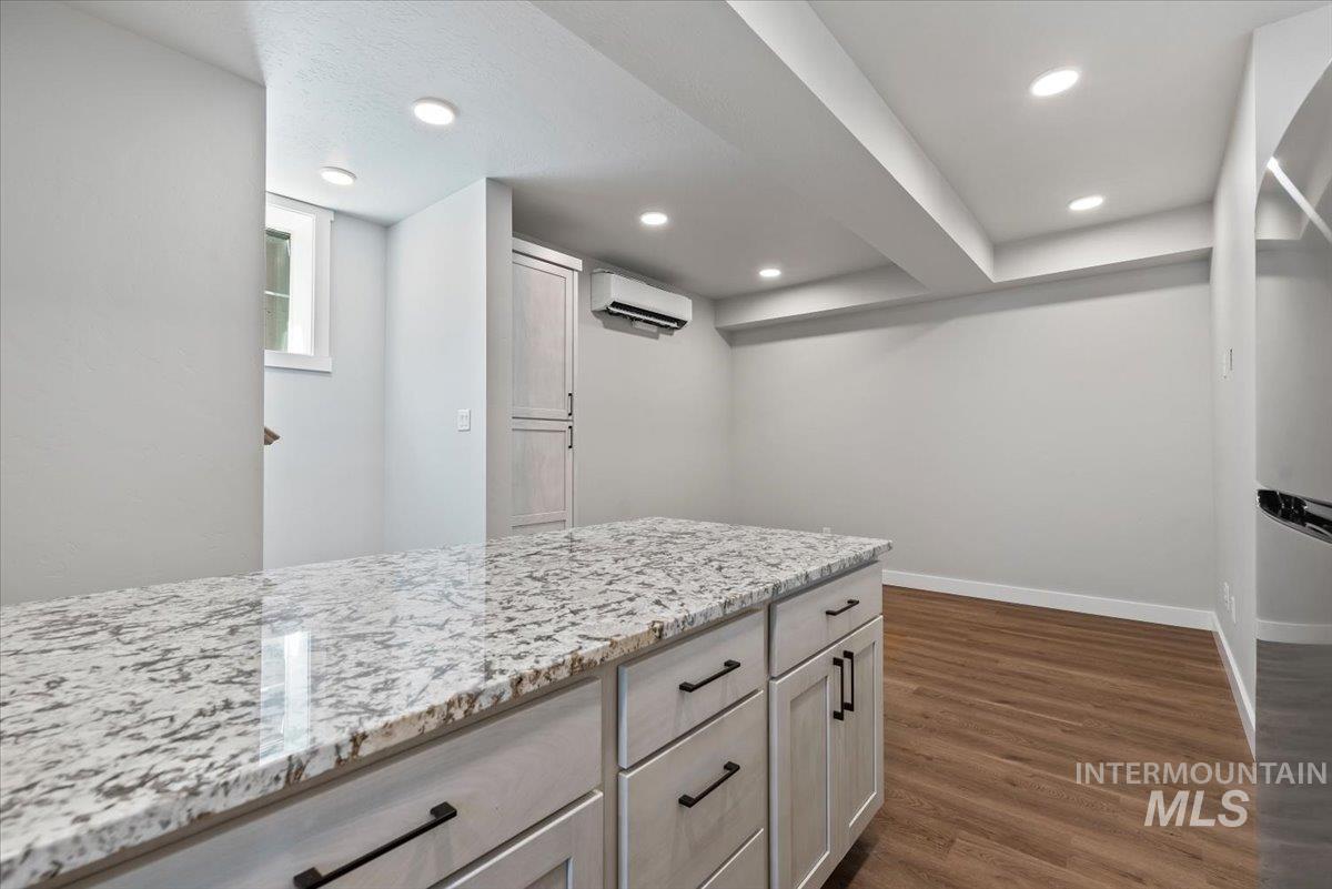 Kitchen featuring a wall unit AC, dark wood finished floors, light stone countertops, recessed lighting, and freestanding refrigerator