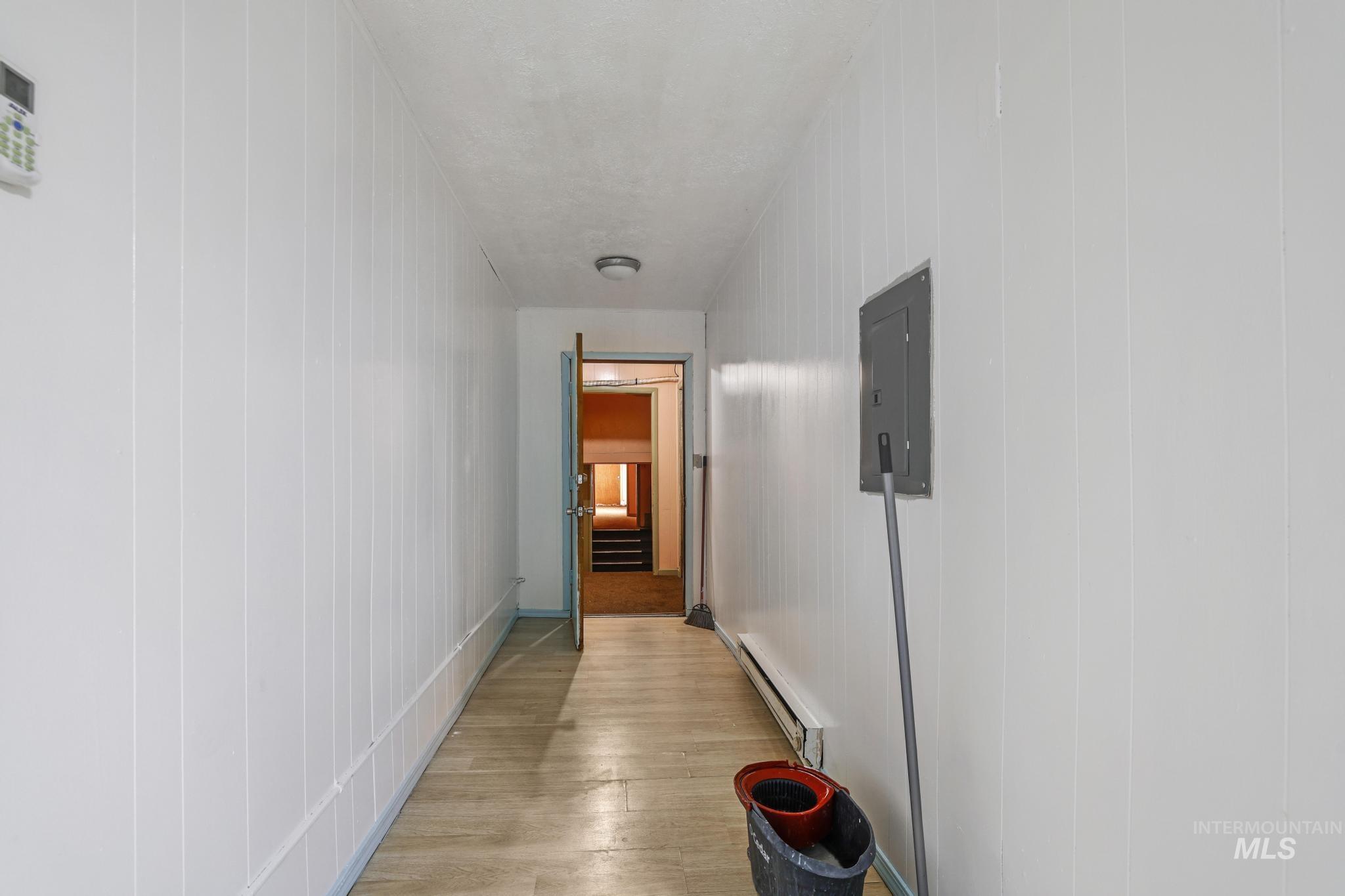Hallway featuring light wood finished floors, a baseboard heating unit, and electric panel