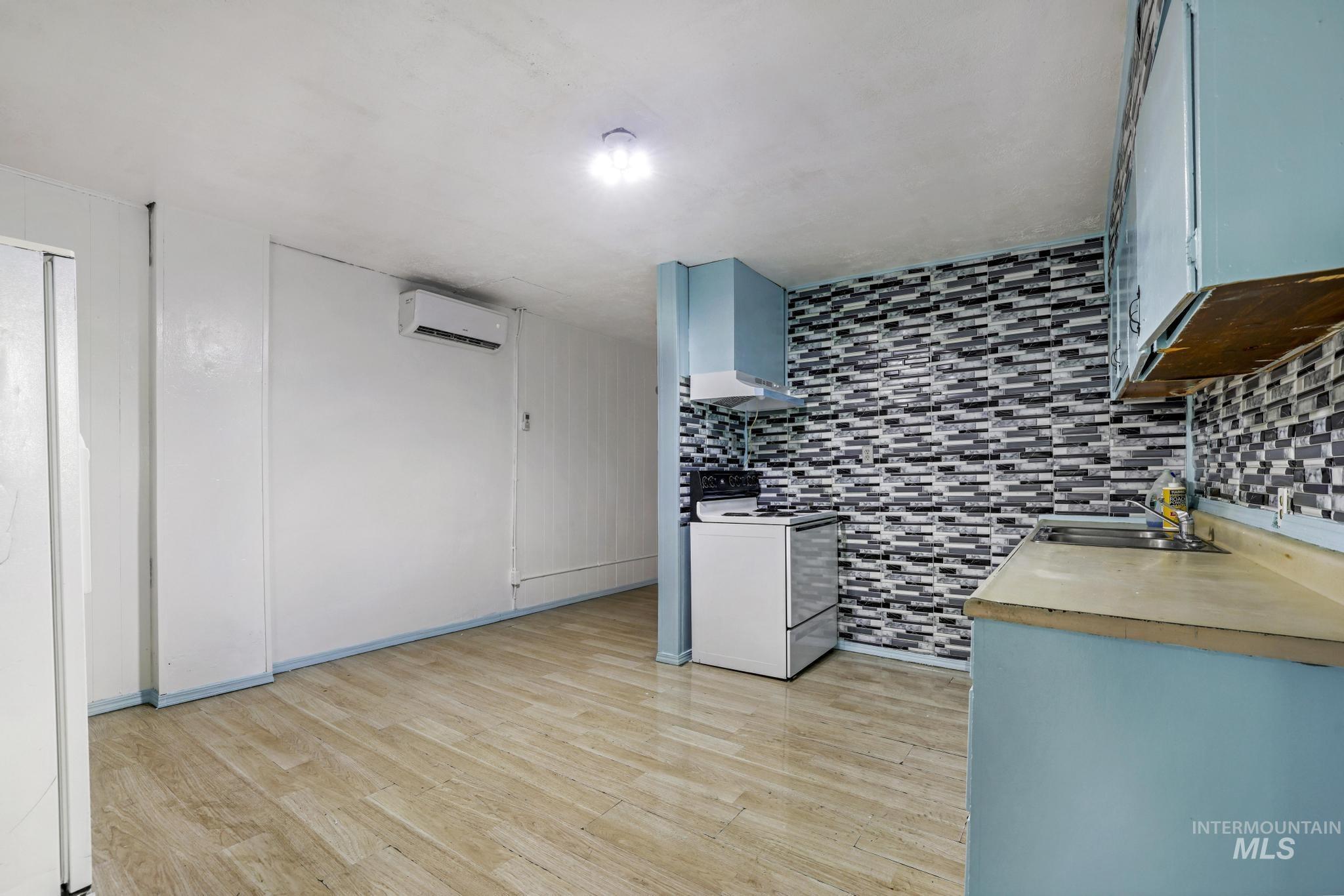 Kitchen with white appliances, light wood-type flooring, wall chimney exhaust hood, wood counters, and a wall unit AC