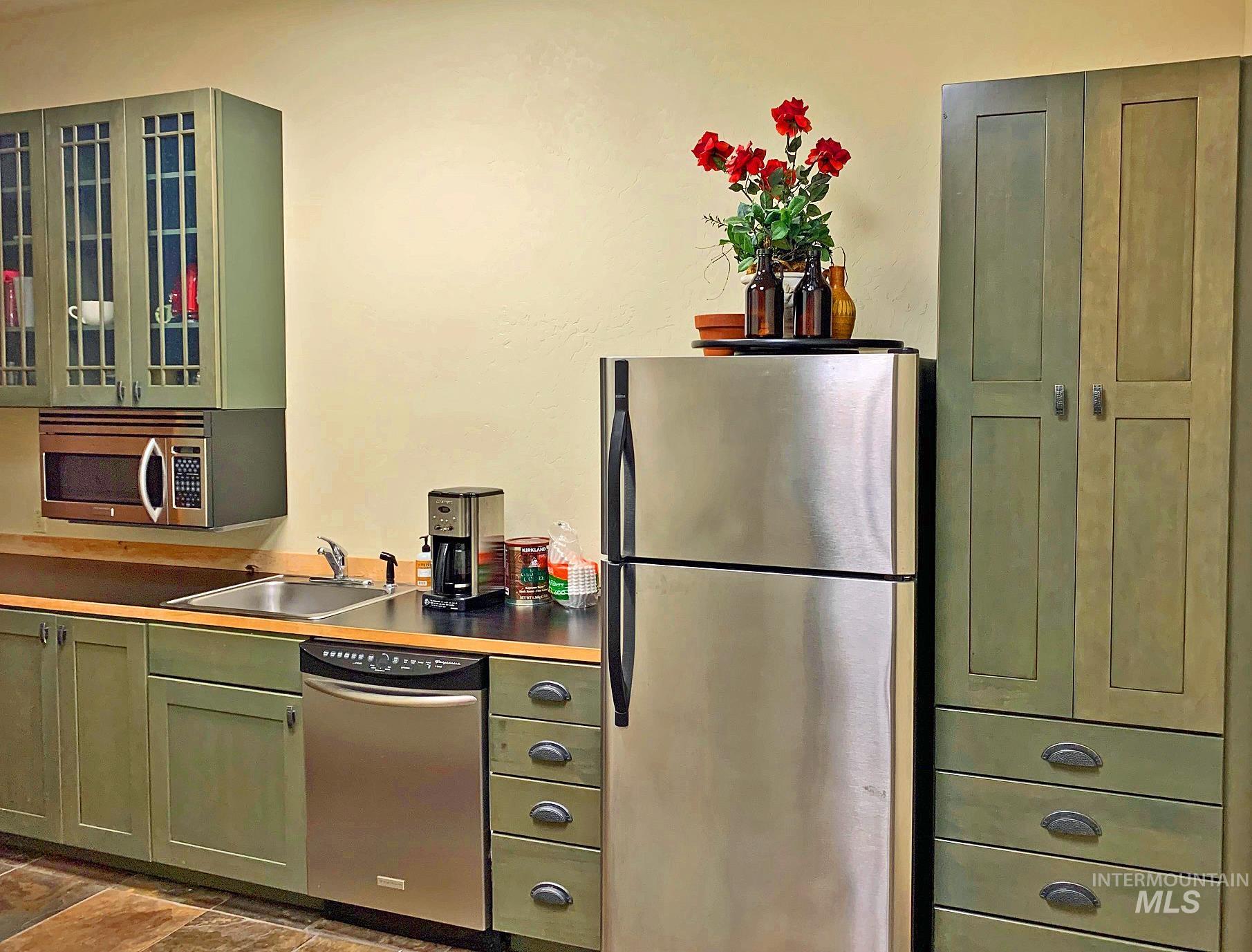 Kitchen with green cabinets, stainless steel appliances, and glass insert cabinets