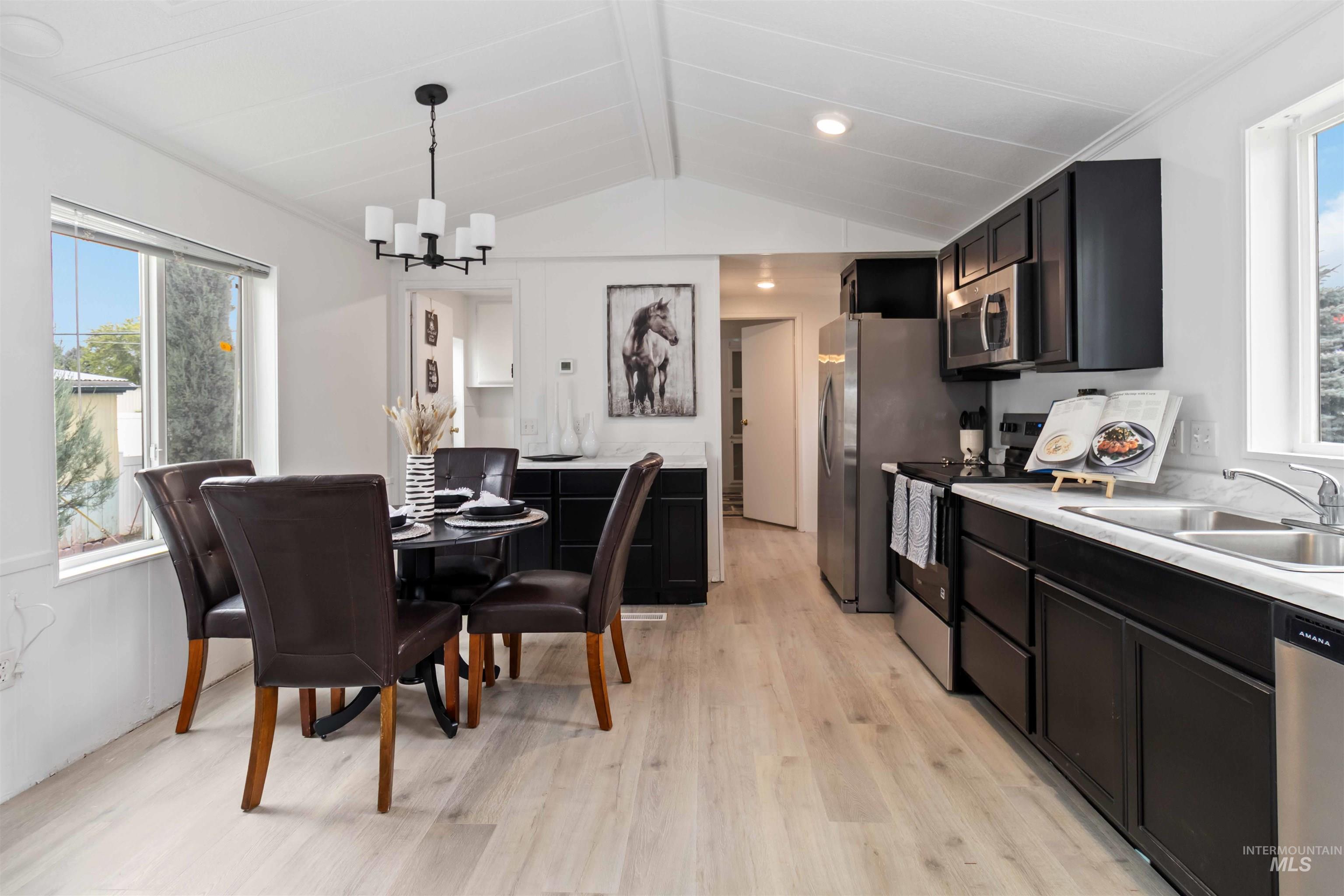 Kitchen featuring dark cabinetry, light countertops, stainless steel appliances, light wood finished floors, and hanging light fixtures