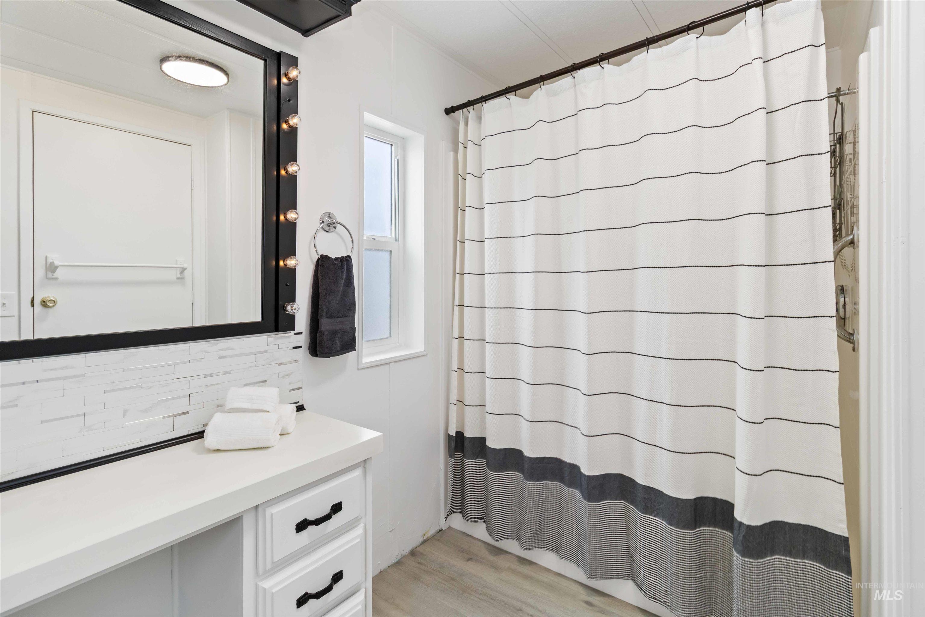 Bathroom with tasteful backsplash, vanity, light wood finished floors, and a shower with shower curtain