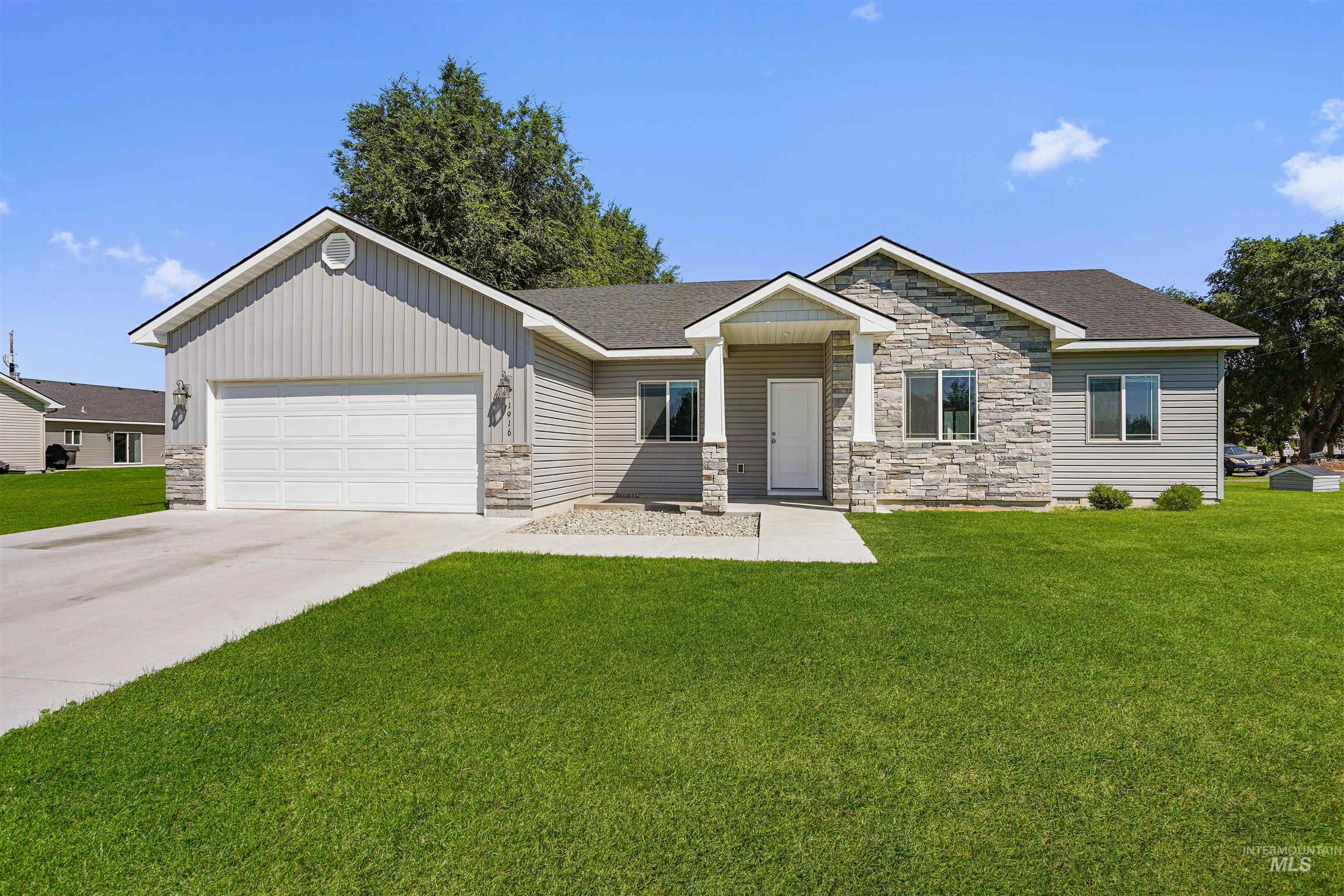 View of front of house with stone siding, driveway, a front yard, and an attached garage