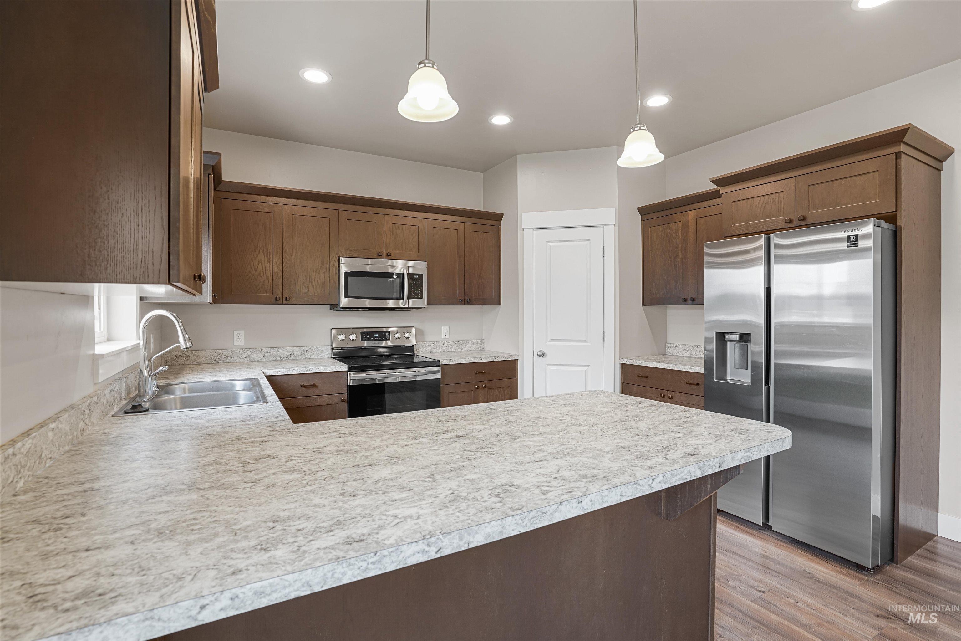 Kitchen featuring appliances with stainless steel finishes, a peninsula, light countertops, decorative light fixtures, and light wood-style floors