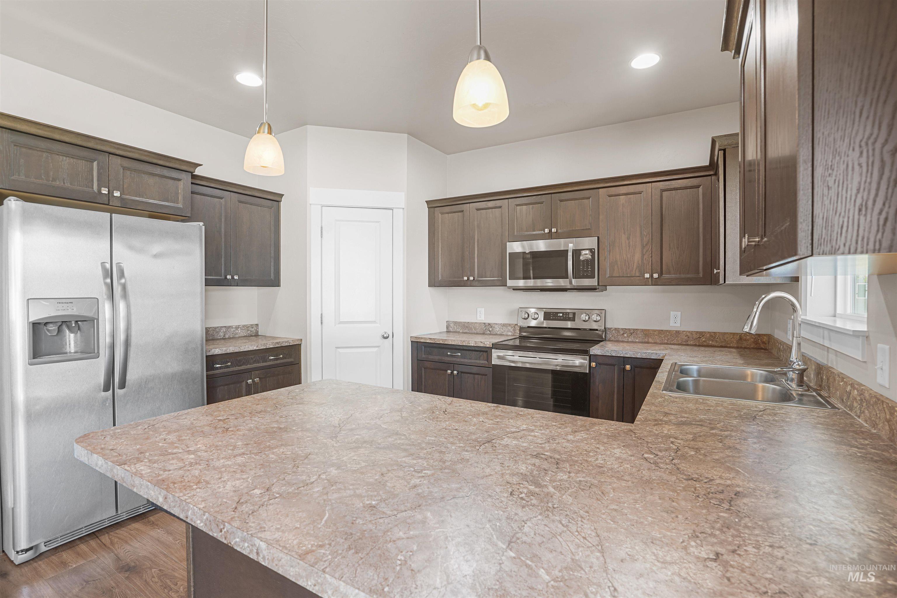 Kitchen with stainless steel appliances, dark brown cabinetry, a peninsula, light countertops, and pendant lighting
