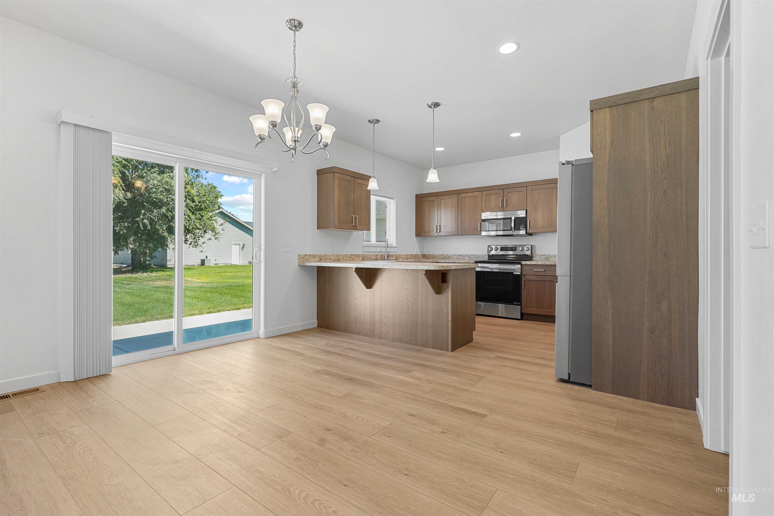 Kitchen featuring a breakfast bar area, recessed lighting, brown cabinets, appliances with stainless steel finishes, and decorative light fixtures