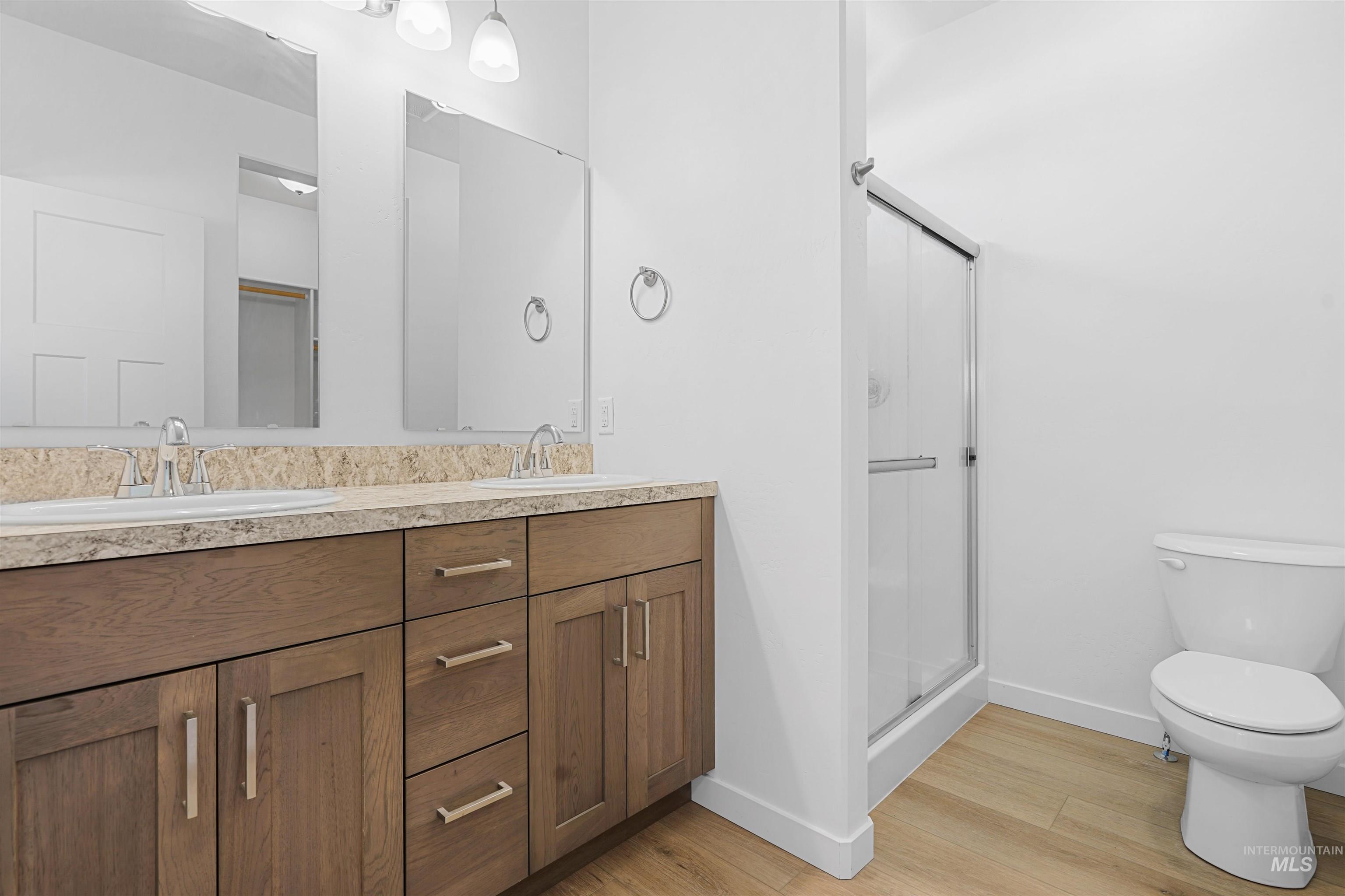 Full bath featuring double vanity, a stall shower, and light wood-type flooring
