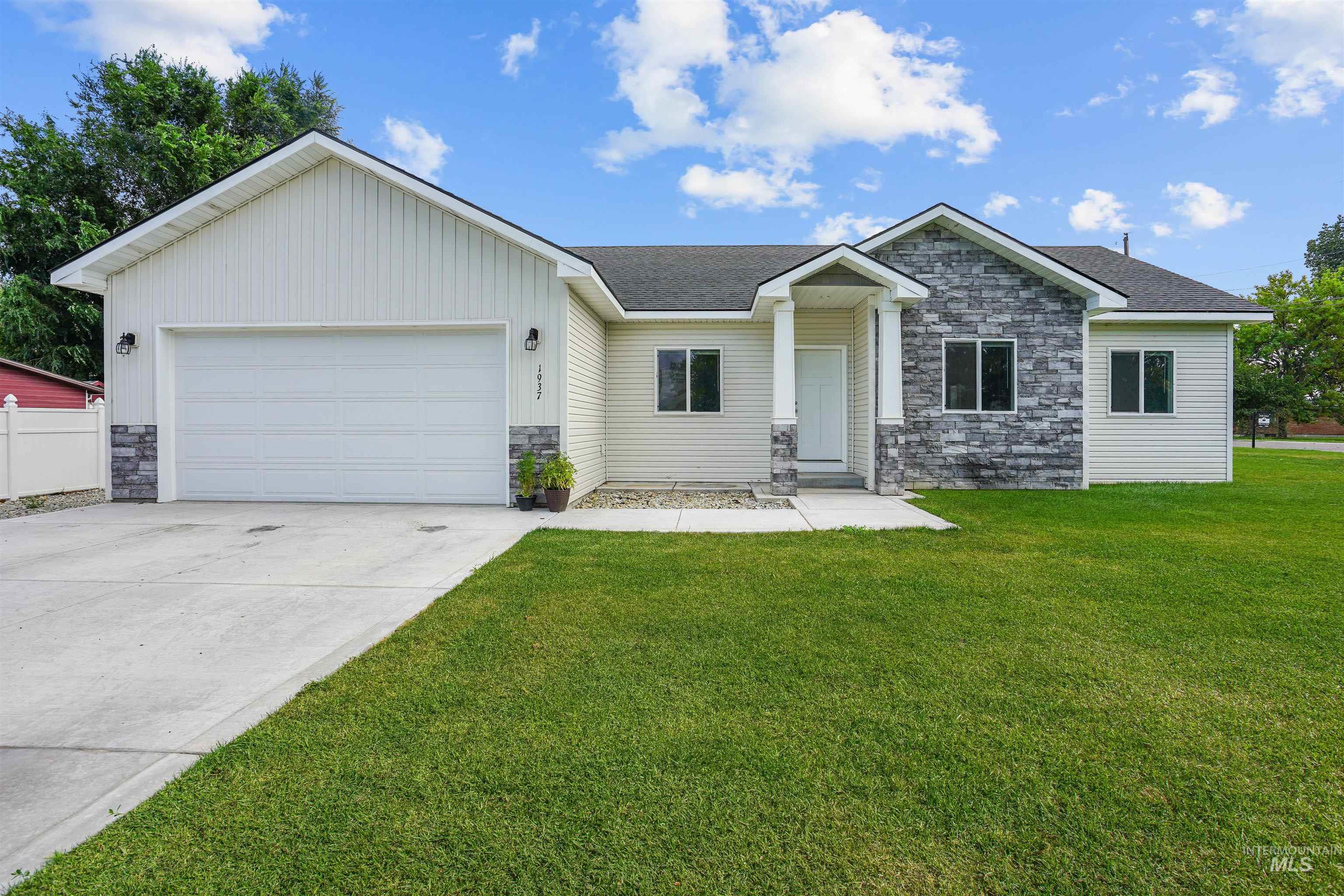 View of front of home with stone siding, driveway, an attached garage, and a front yard