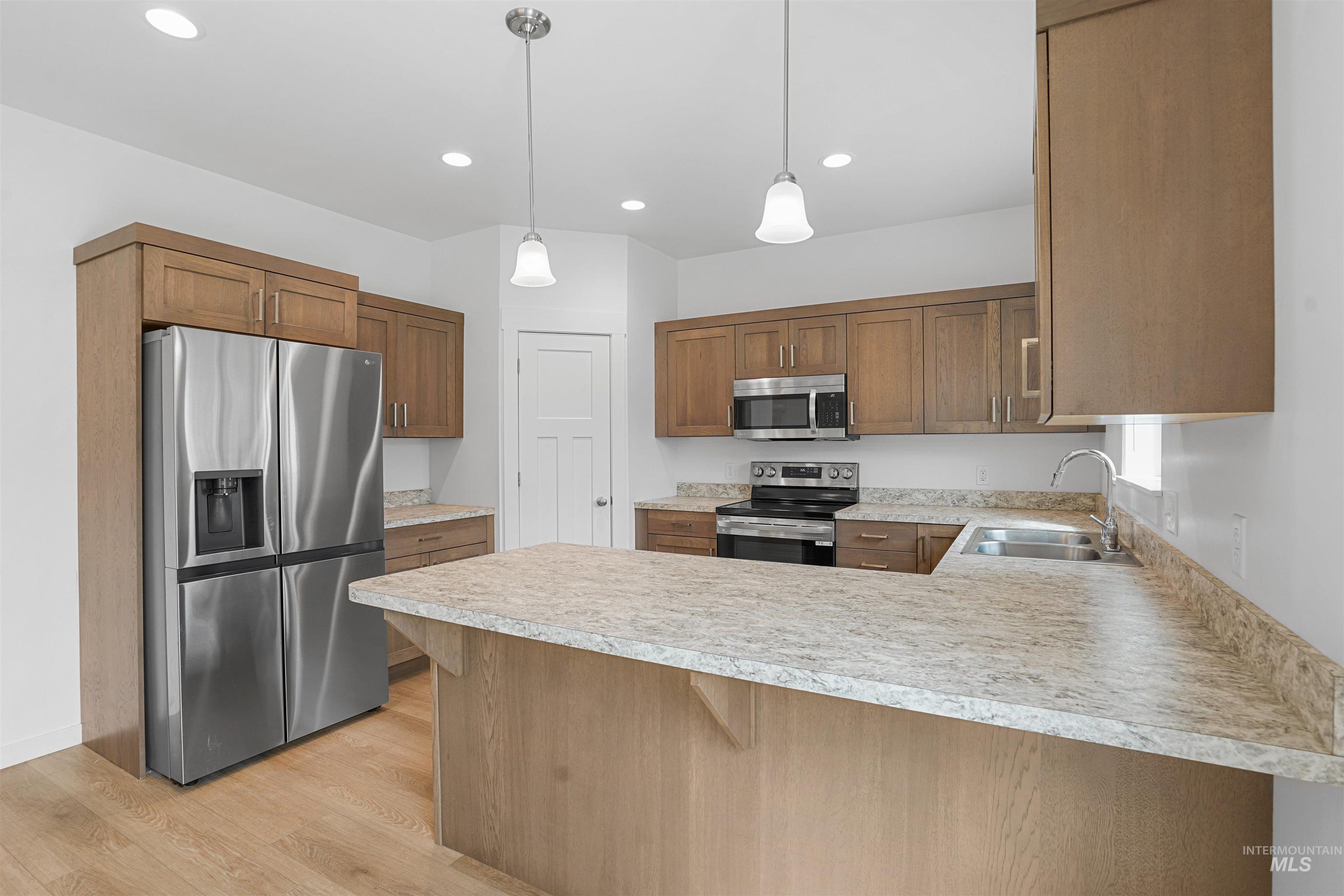Kitchen with a peninsula, appliances with stainless steel finishes, light countertops, pendant lighting, and light wood finished floors