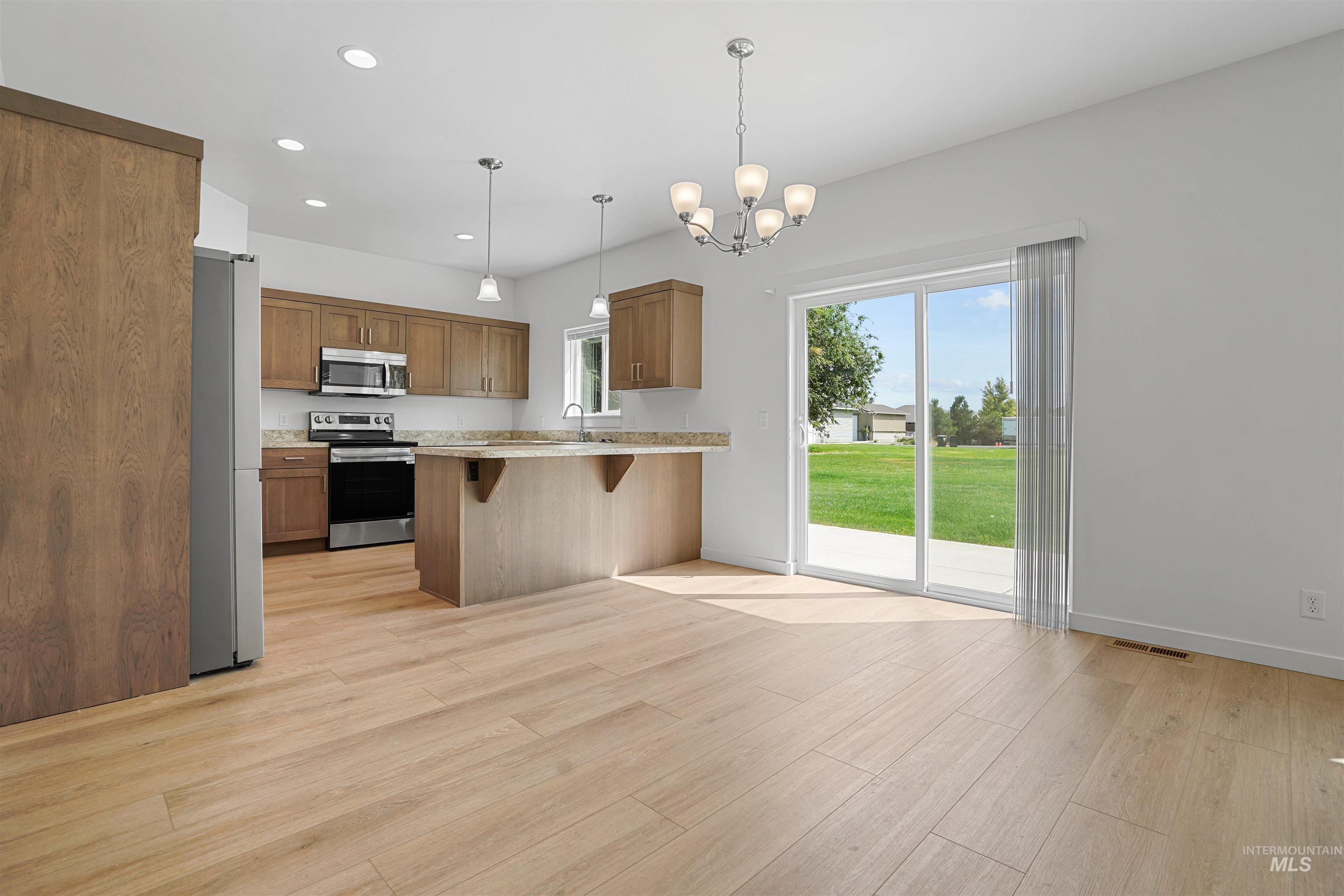 Kitchen with a breakfast bar area, appliances with stainless steel finishes, brown cabinetry, recessed lighting, and pendant lighting