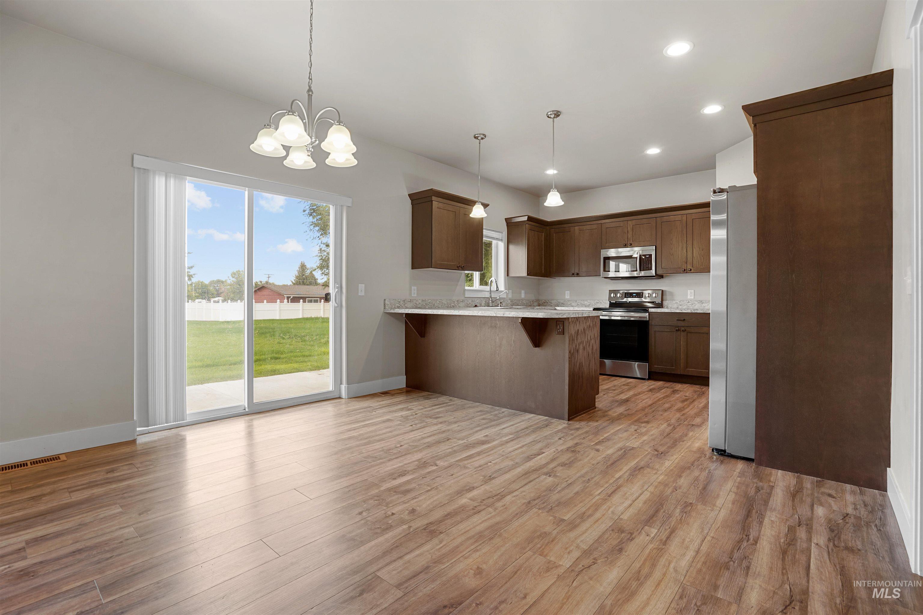 Kitchen featuring recessed lighting, a breakfast bar area, pendant lighting, appliances with stainless steel finishes, and light wood finished floors