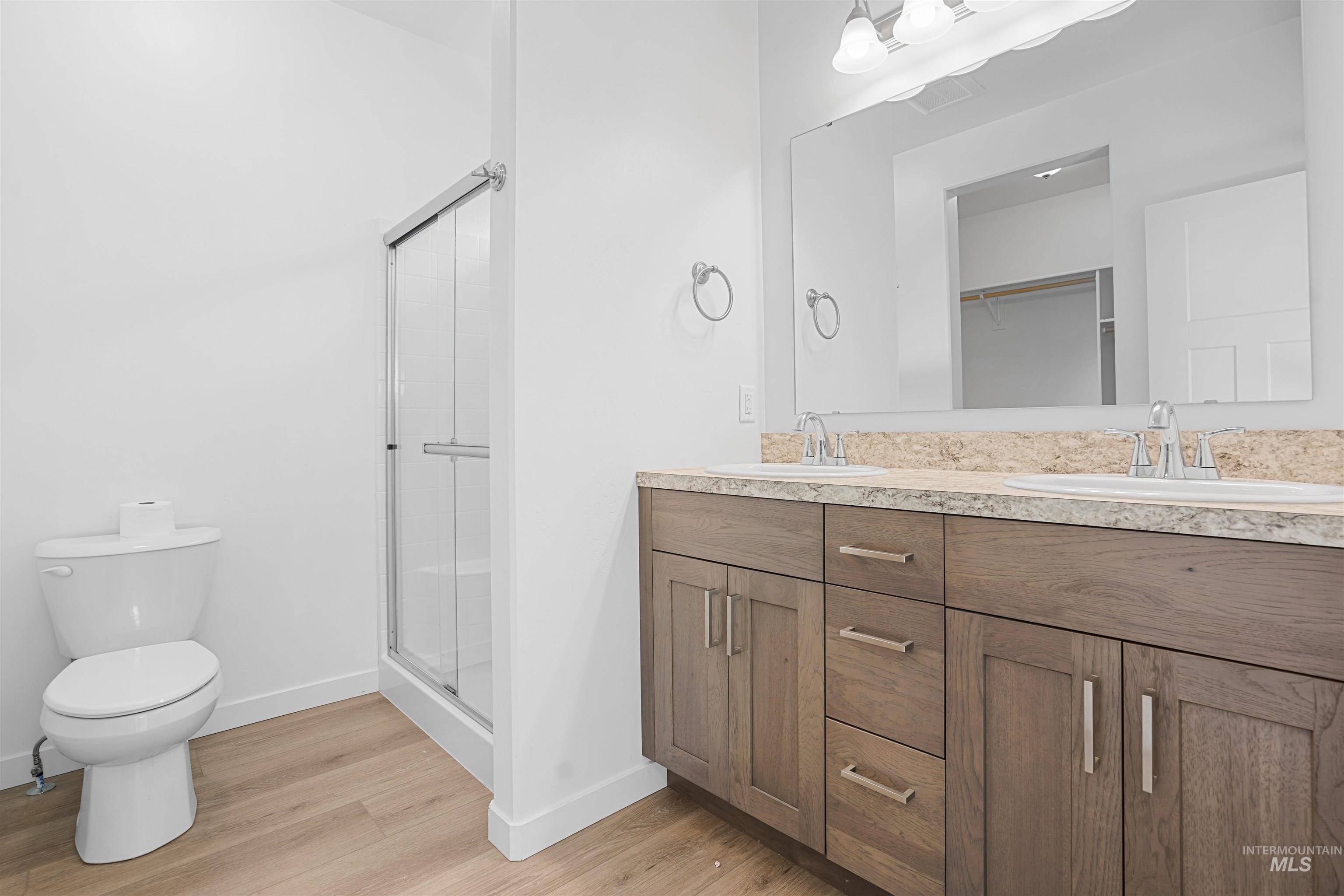 Bathroom featuring a stall shower, double vanity, light wood-type flooring, and a spacious closet