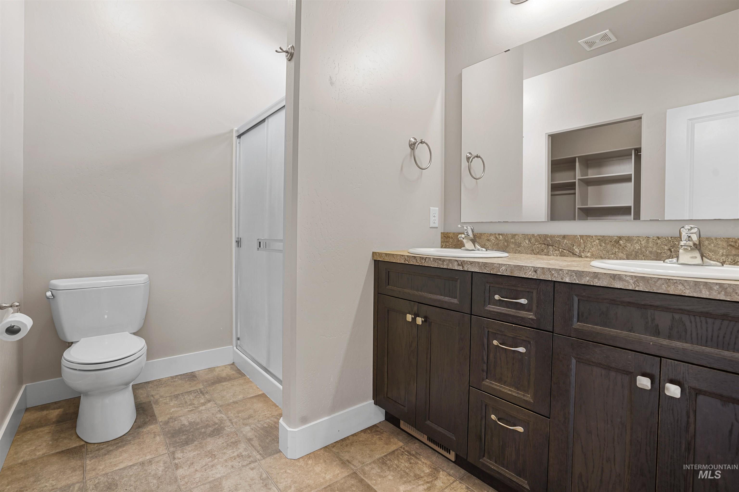 Full bathroom with a stall shower, double vanity, and a walk in closet