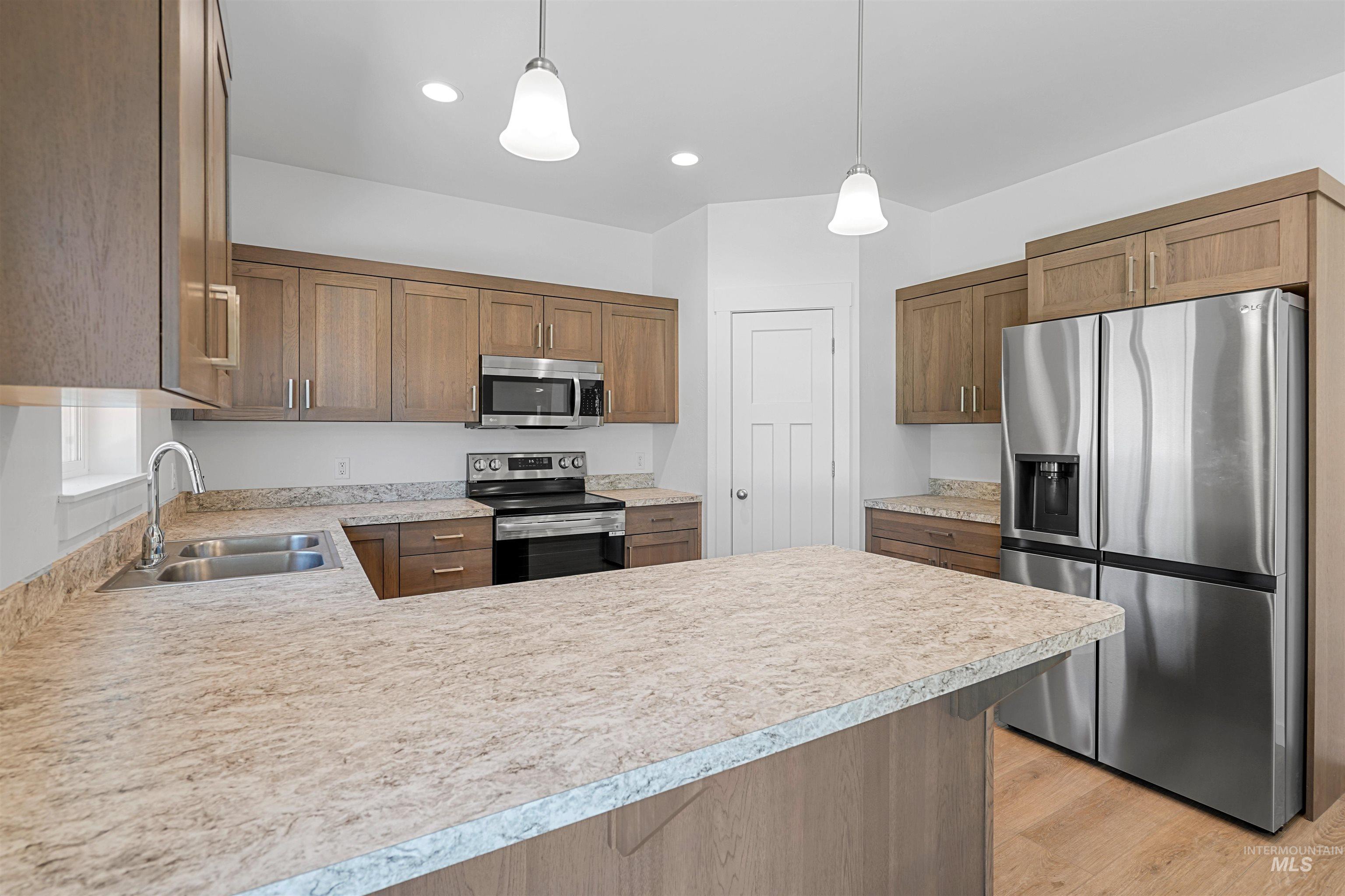 Kitchen featuring stainless steel appliances, a peninsula, decorative light fixtures, light countertops, and recessed lighting