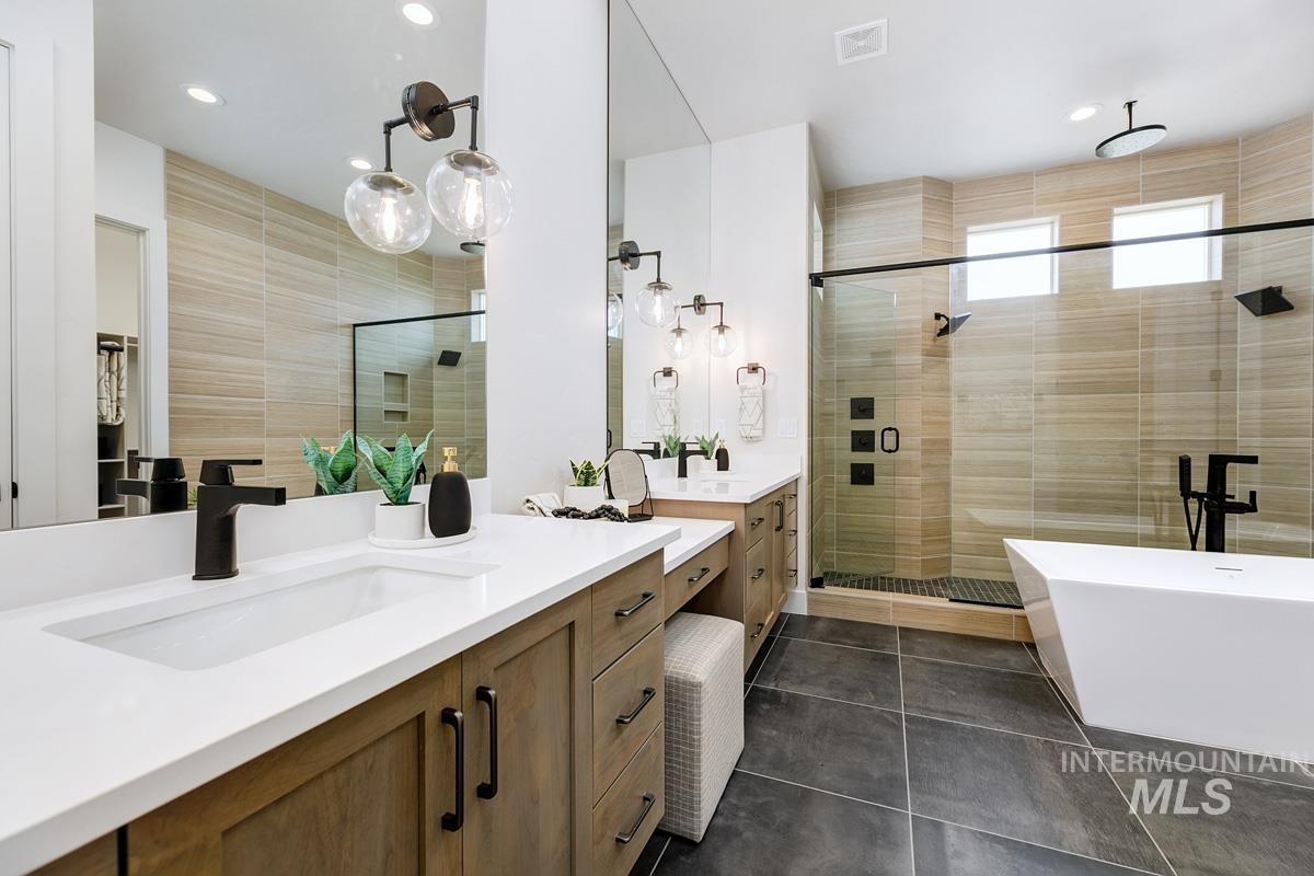 Bathroom featuring a stall shower, two vanities, dark tile patterned floors, a freestanding bath, and tile walls
