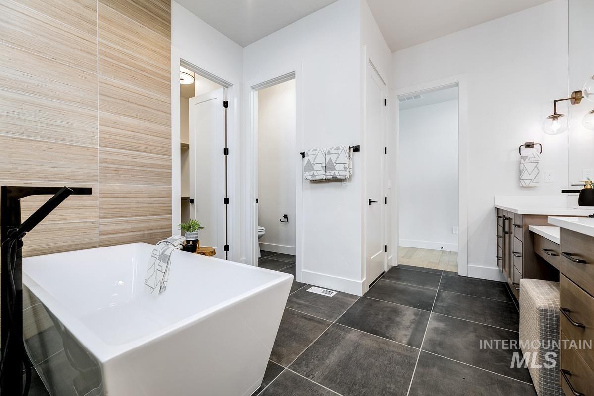 Bathroom featuring vanity, a soaking tub, dark tile patterned floors, and tile walls