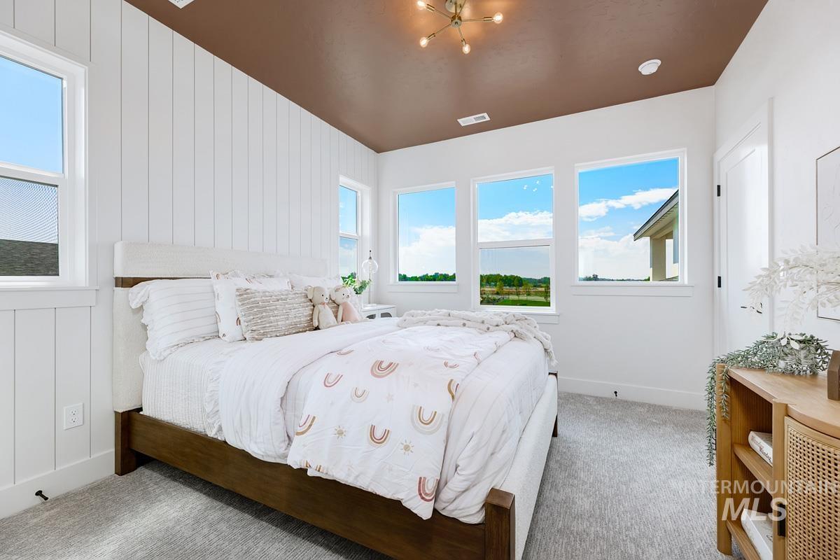 Bedroom with multiple windows, carpet floors, wooden walls, and a chandelier