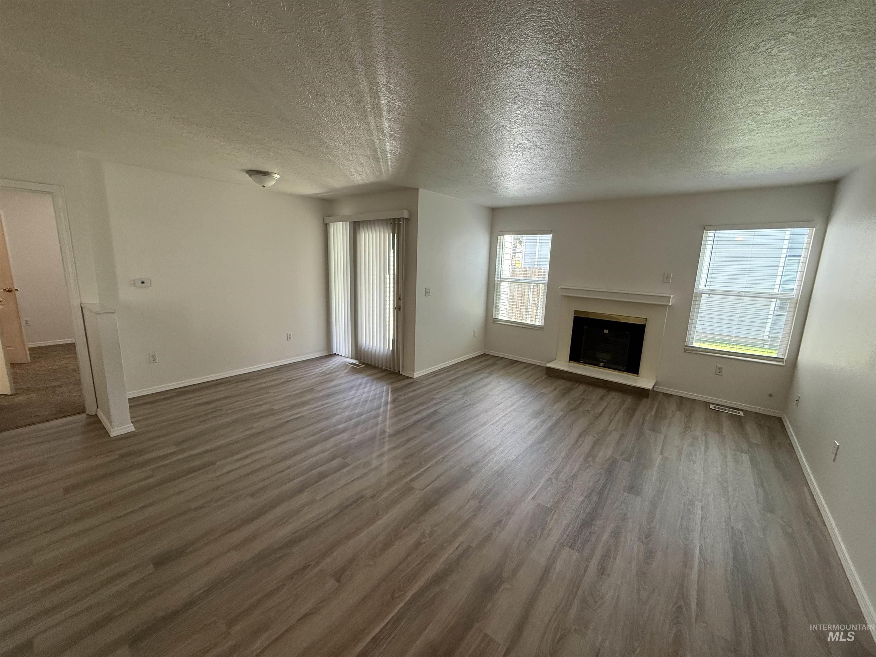 Unfurnished living room with a textured ceiling, a fireplace with raised hearth, and wood finished floors