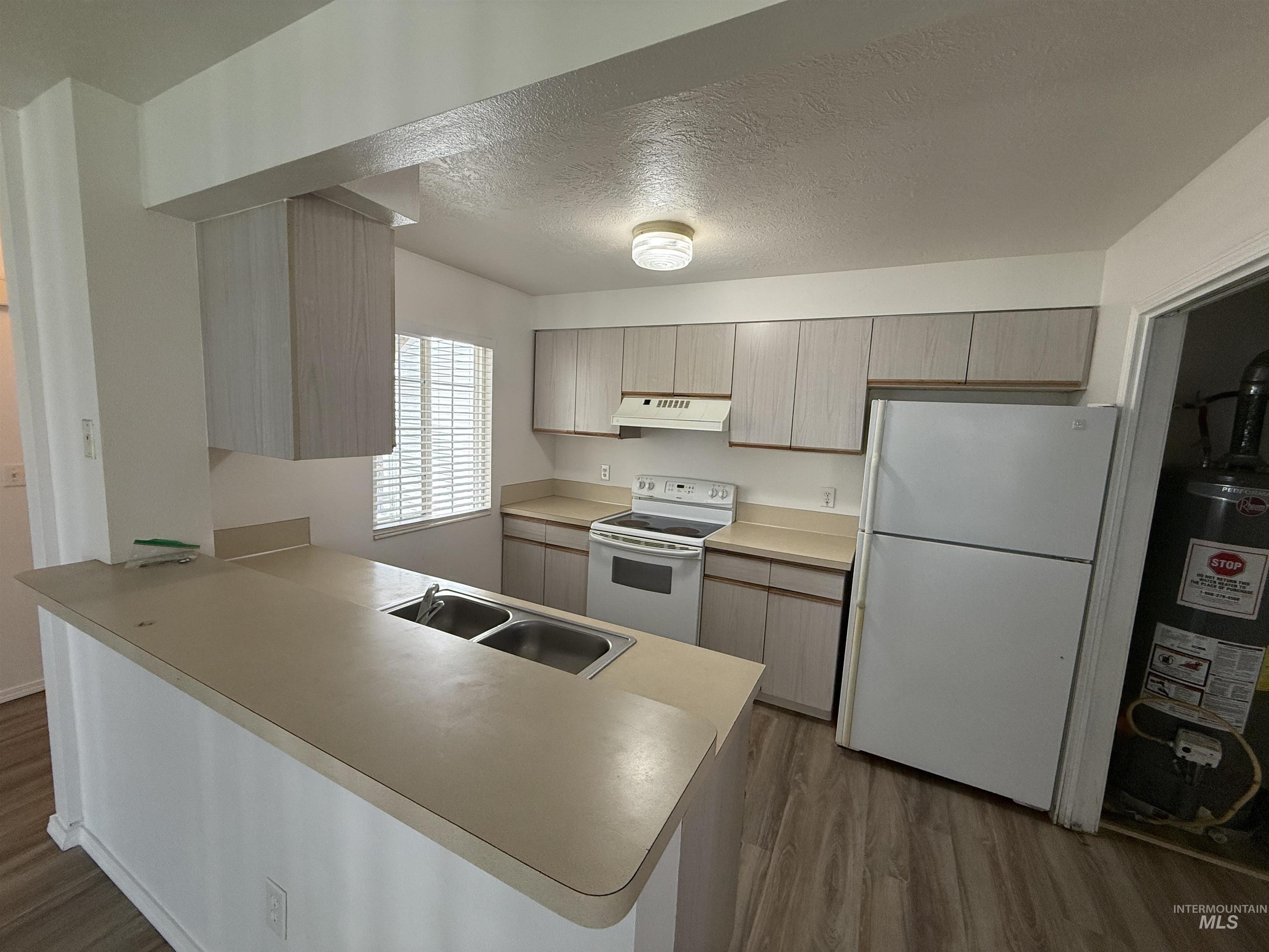 Kitchen featuring a peninsula, a textured ceiling, white appliances, dark wood finished floors, and light countertops
