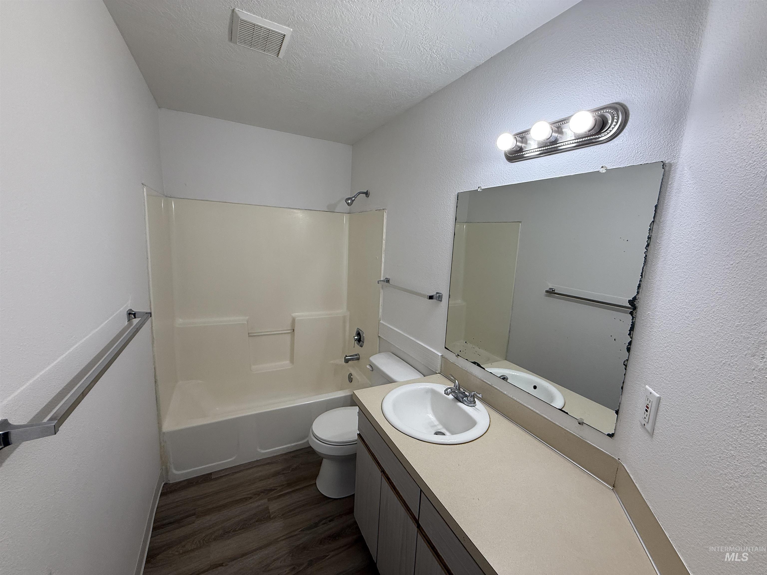 Bathroom with dark wood-type flooring, shower / bathtub combination, vanity, a textured ceiling, and a textured wall