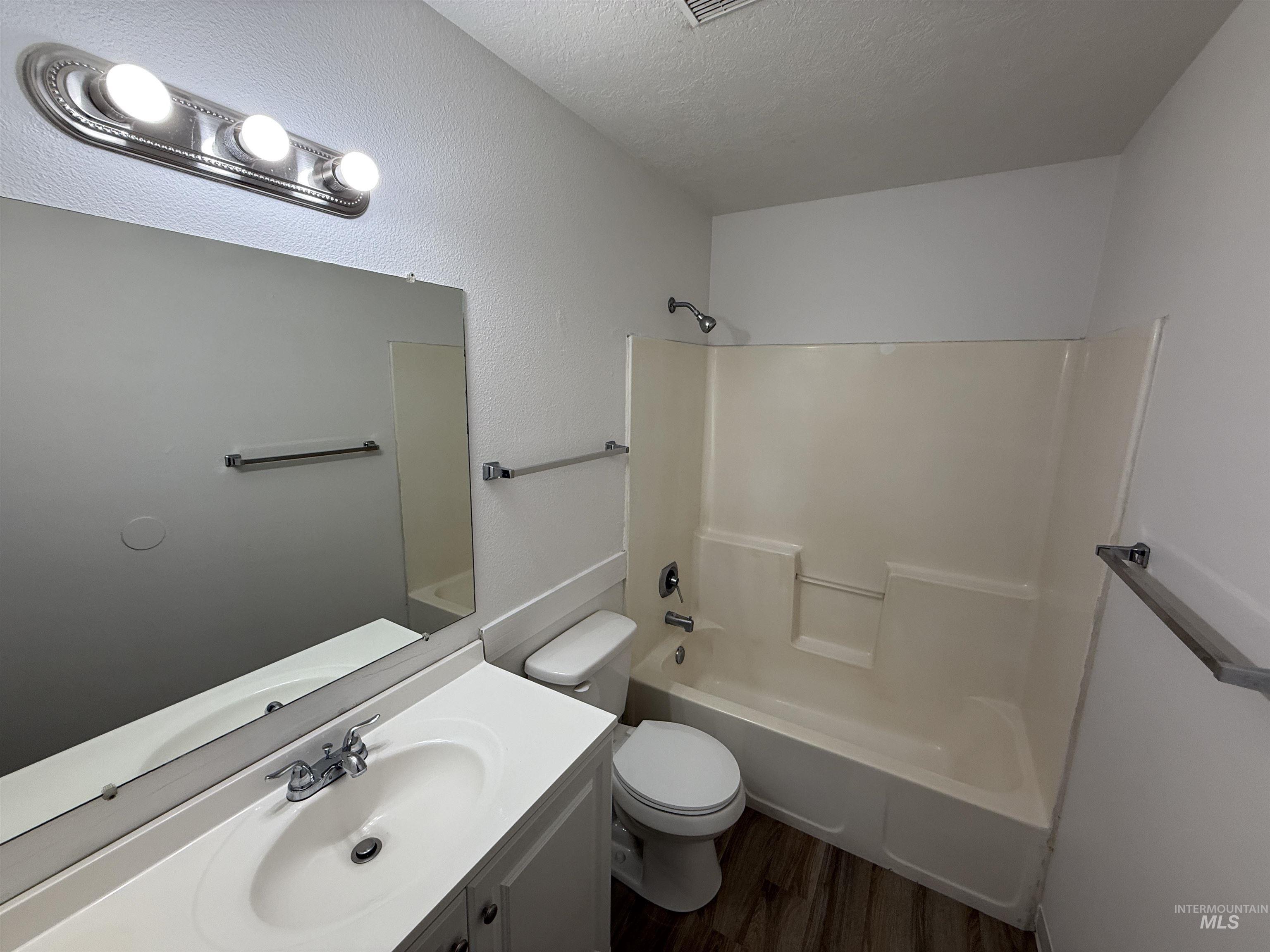 Full bathroom with tub / shower combination, dark wood-type flooring, vanity, and a textured ceiling