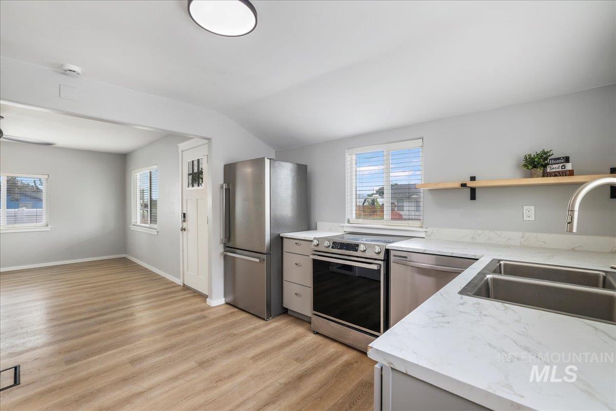 Kitchen featuring light wood-type flooring, appliances with stainless steel finishes, lofted ceiling, and open shelves