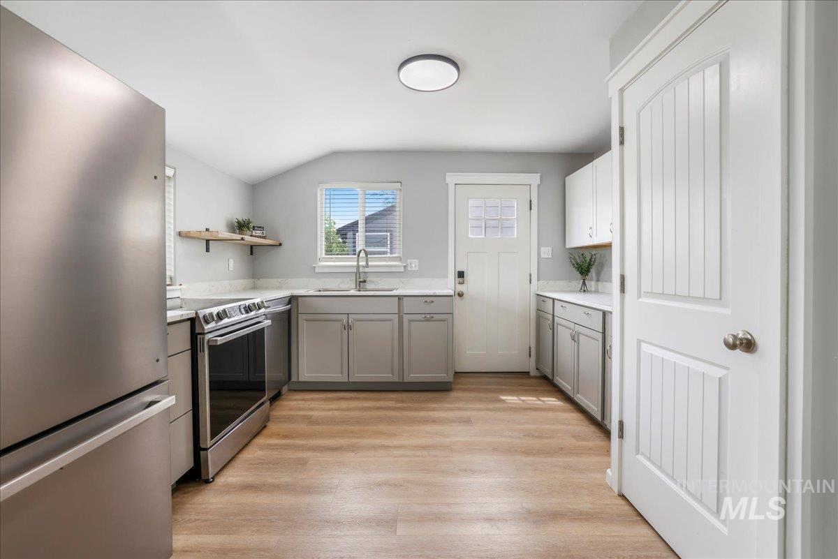 Kitchen with gray cabinets, appliances with stainless steel finishes, open shelves, light wood-style floors, and lofted ceiling