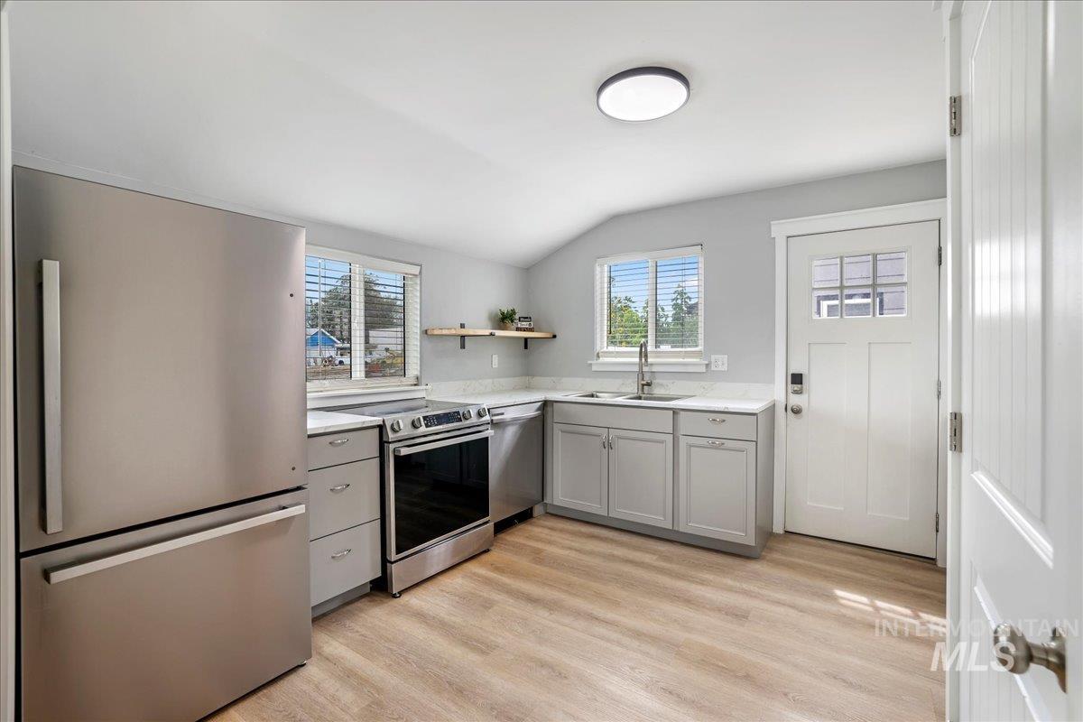Kitchen with stainless steel appliances, gray cabinets, healthy amount of natural light, open shelves, and vaulted ceiling