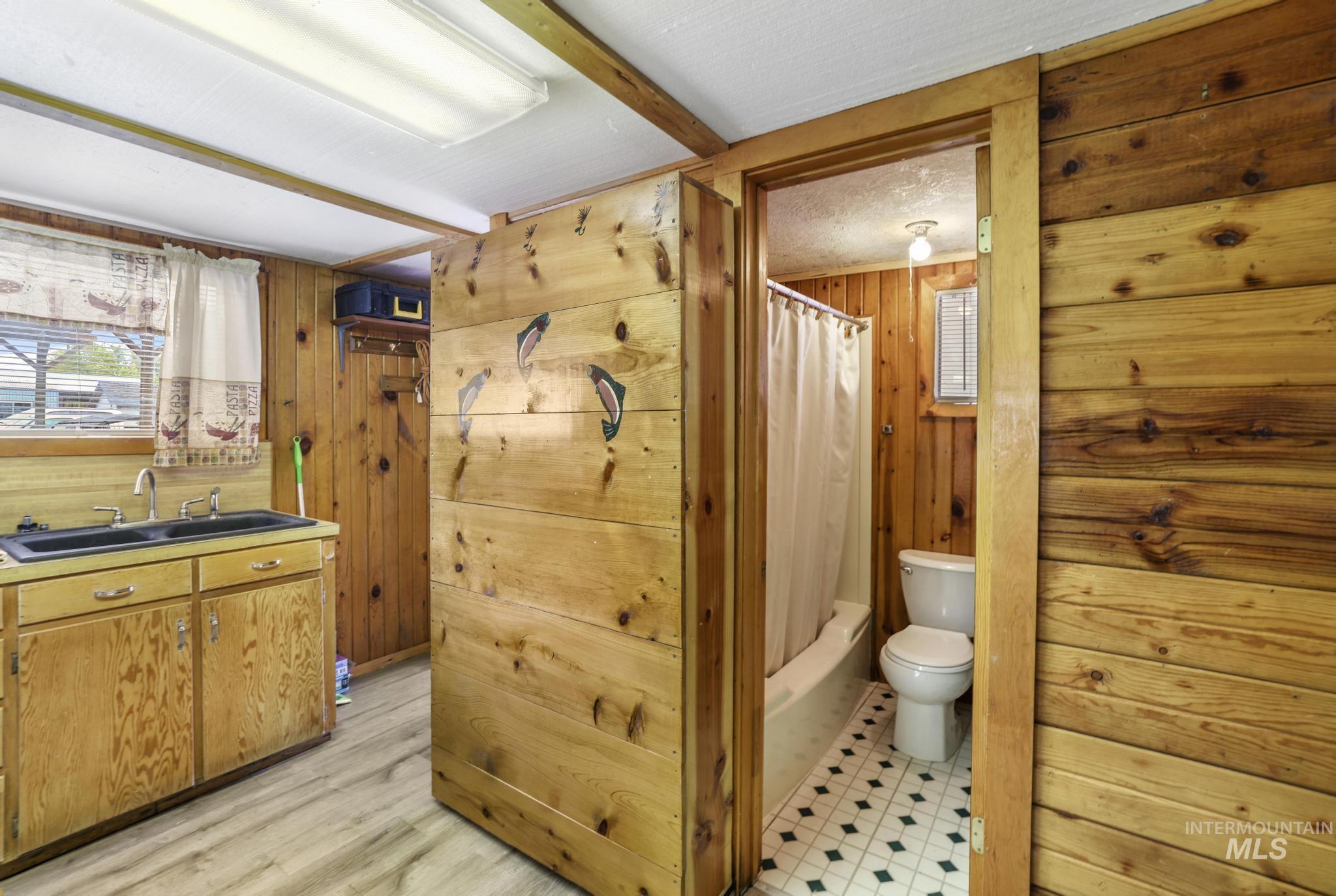 Full bath with wood walls, vanity, shower / bathtub combination with curtain, and light wood-style floors