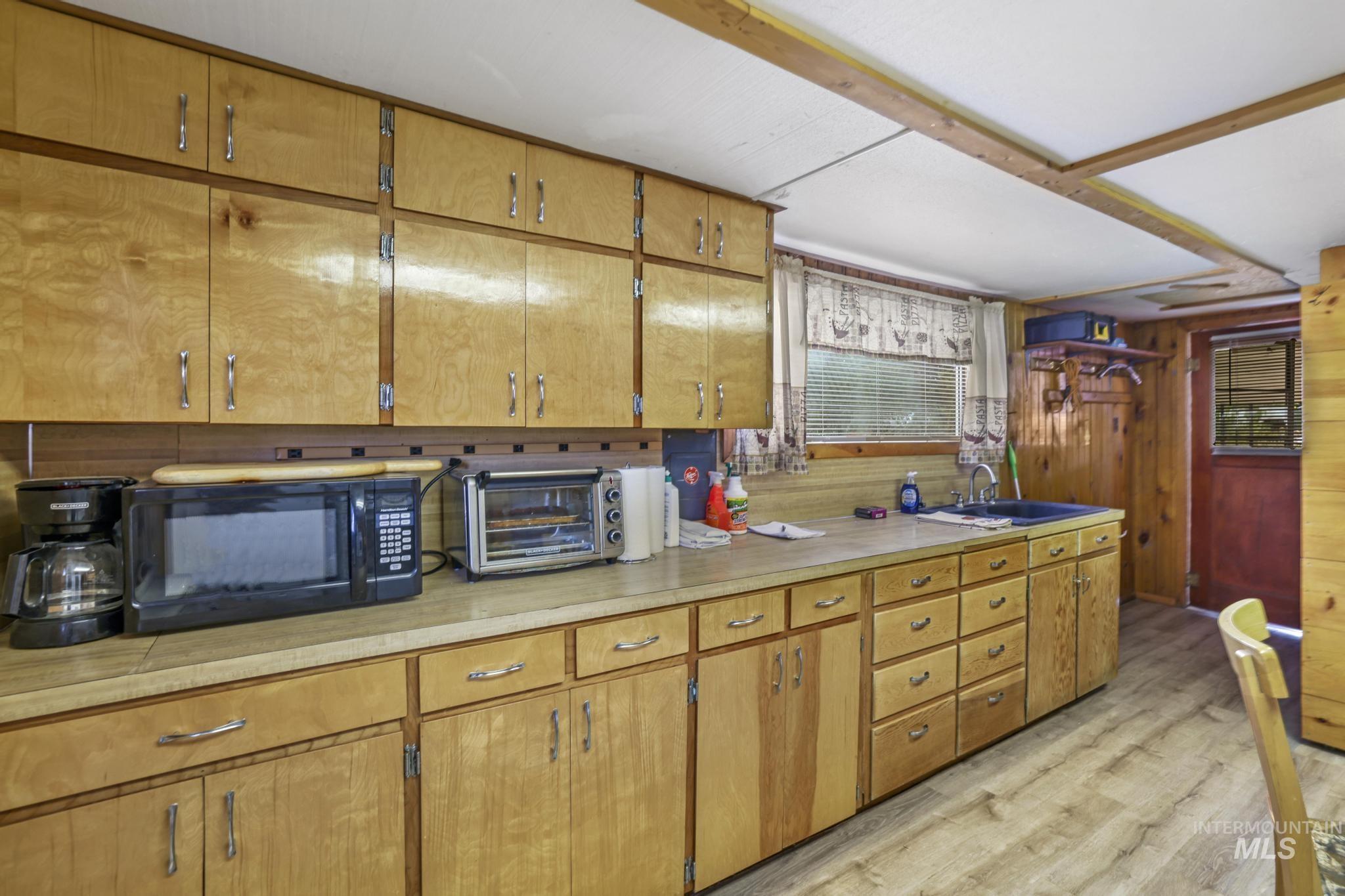 Kitchen with light countertops, light floors, brown cabinets, black microwave, and wood walls