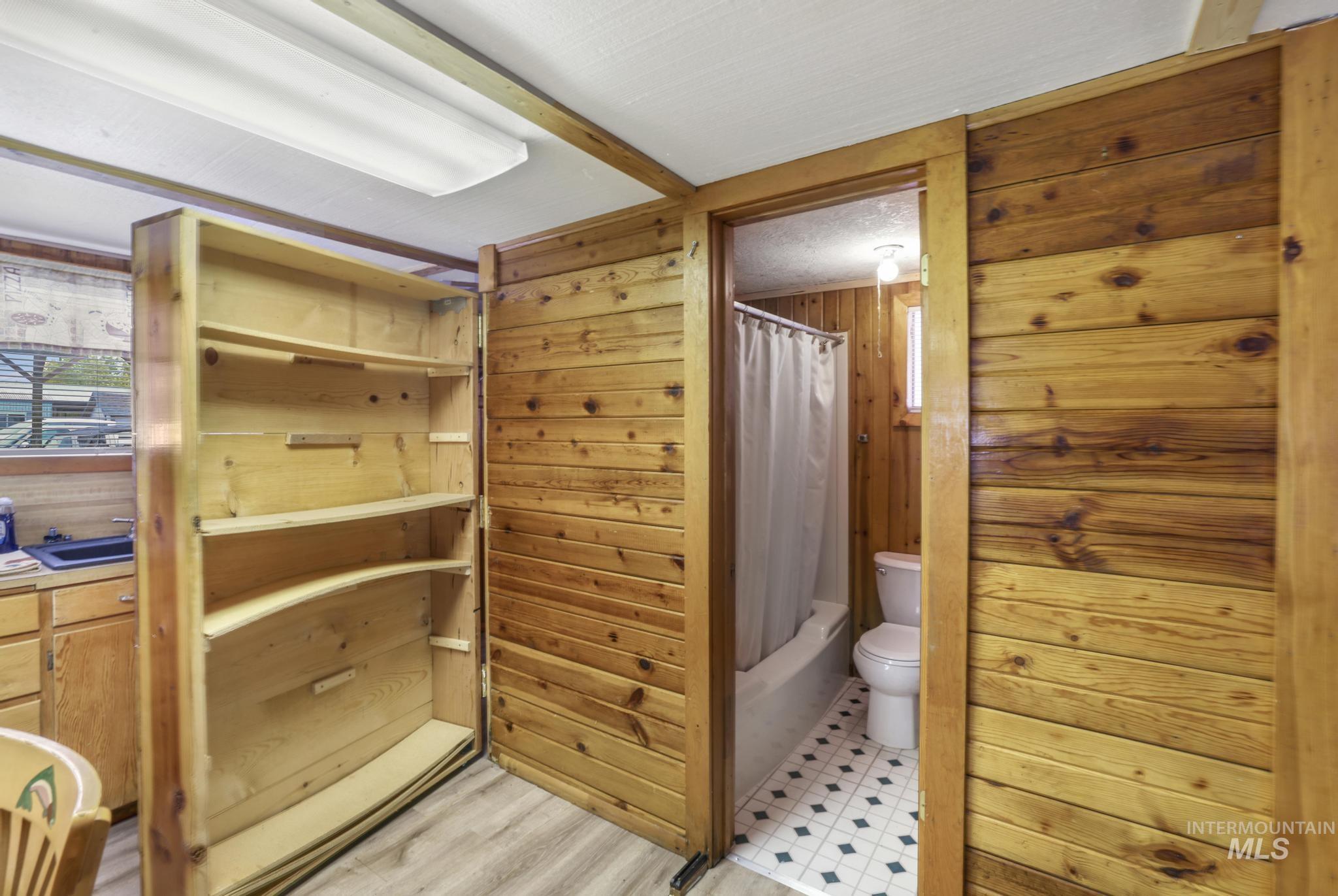 Full bathroom featuring wood walls and shower / tub combo. Hidden pantry.
