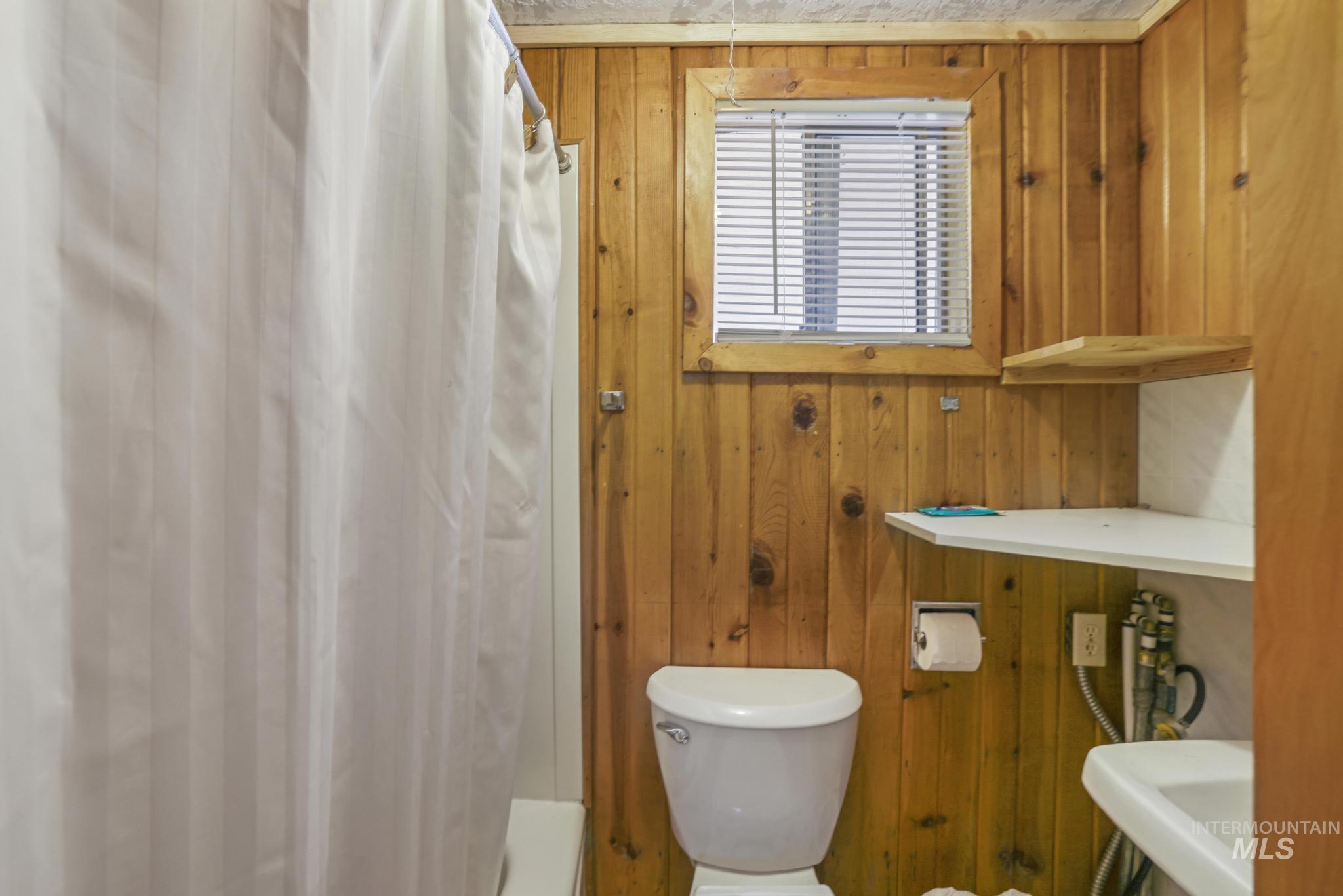 Full bathroom with wood walls and shower / tub combo with curtain - water heater.