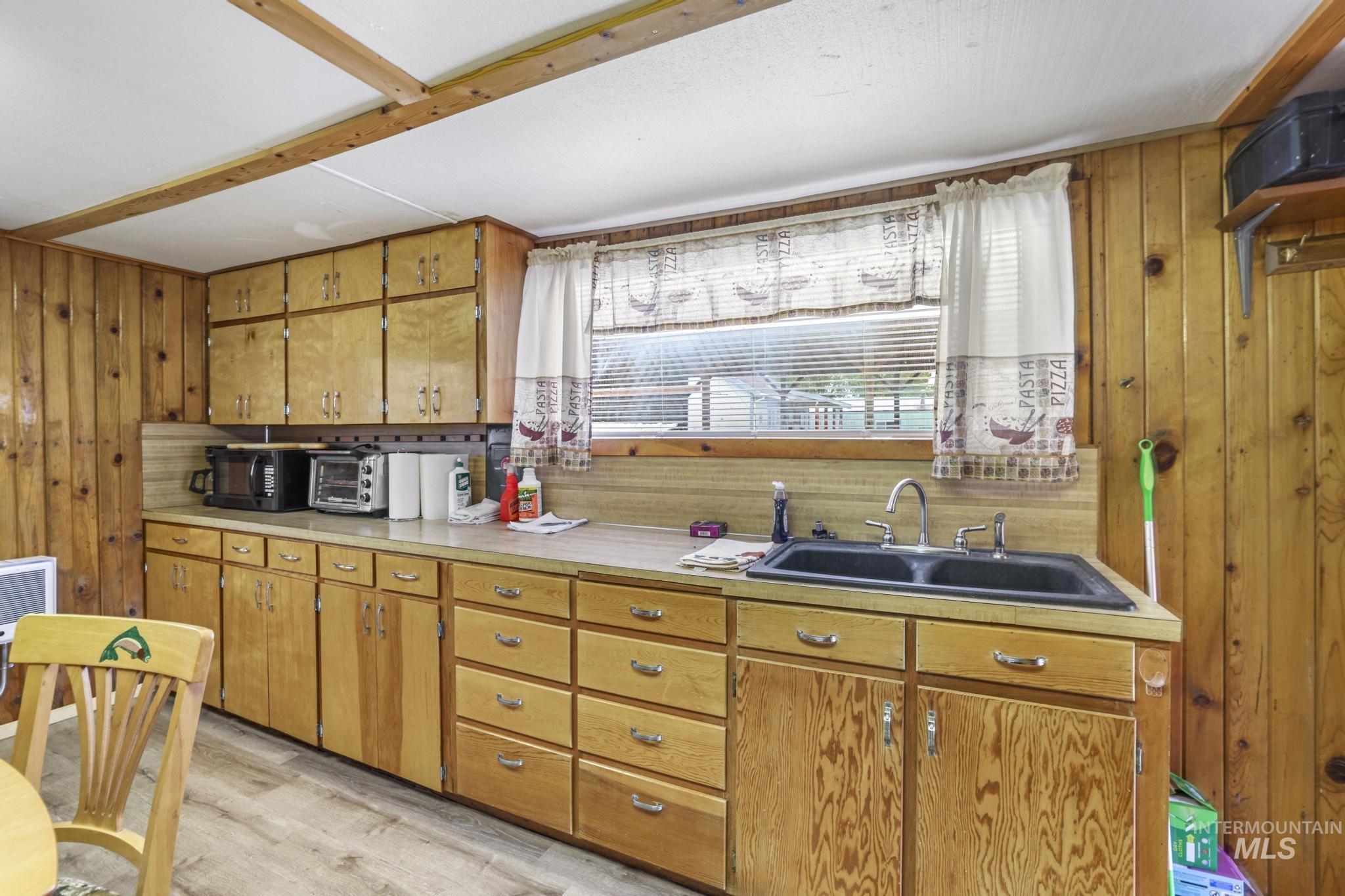 Kitchen with wooden walls, light countertops, light wood-style floors, brown cabinetry, and black microwave