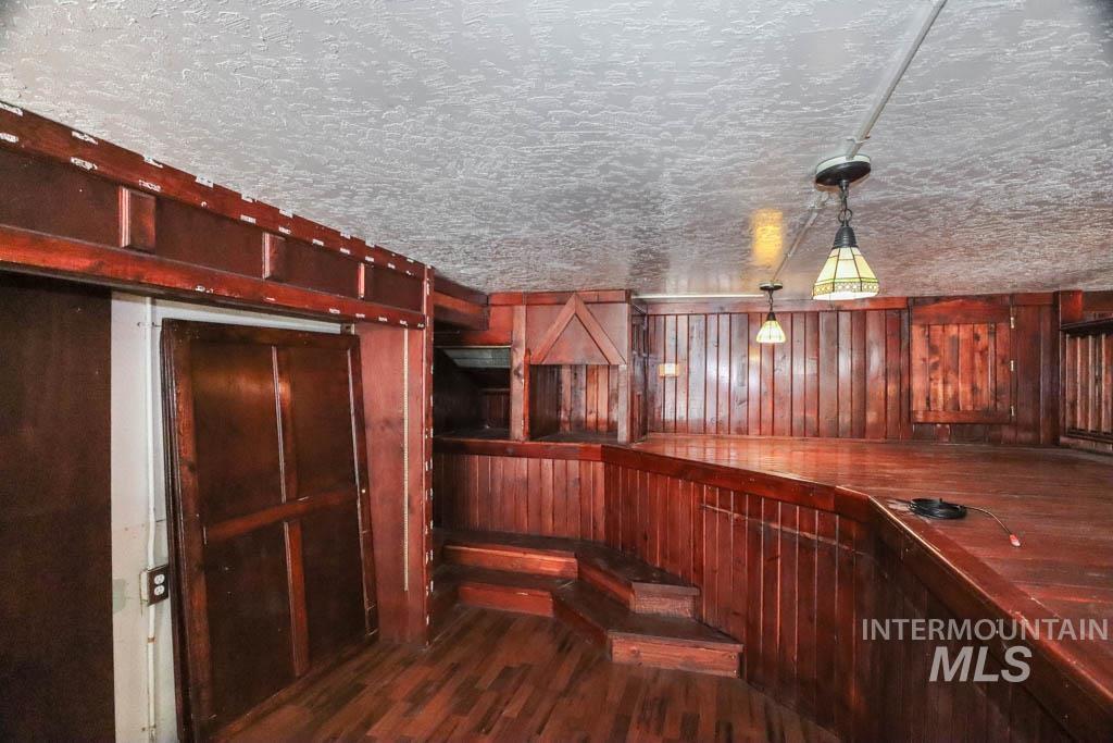 Bar area with dark wood-type flooring, hanging light fixtures, a textured ceiling, and wood walls