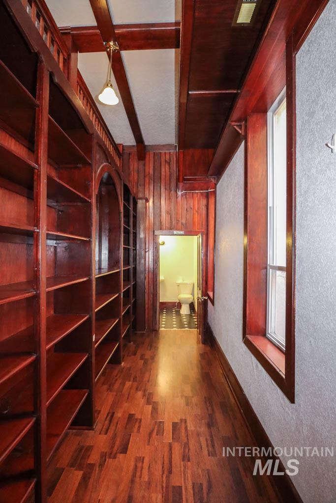 Wine area with dark wood-style flooring, wood walls, beam ceiling, and a textured wall