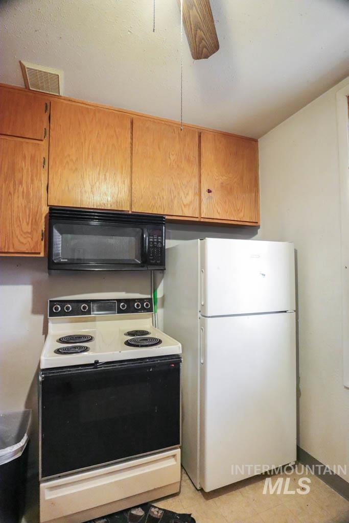 Kitchen with range with electric stovetop, black microwave, freestanding refrigerator, brown cabinetry, and light countertops